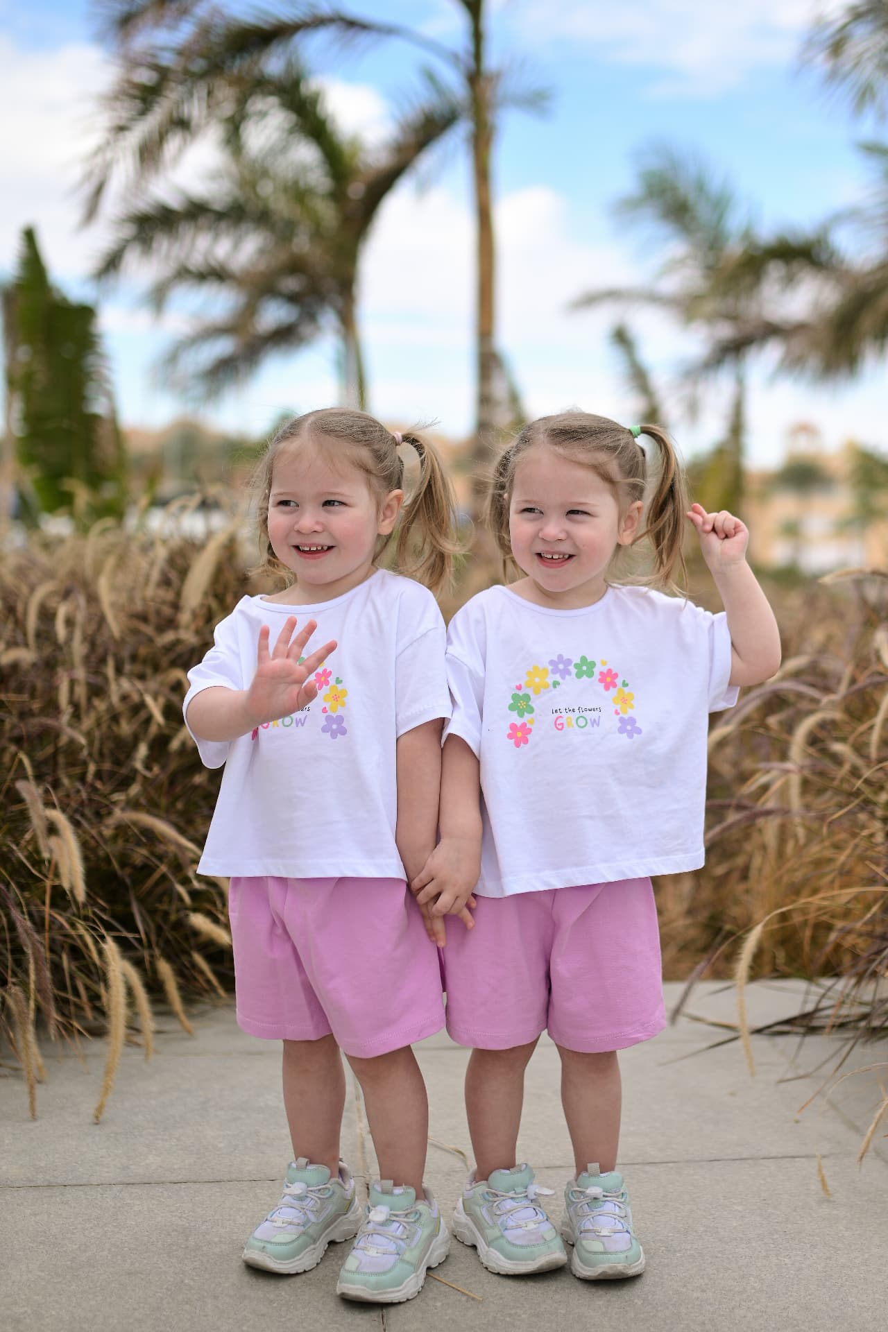 Twin girls in matching white tops and pink shorts waving