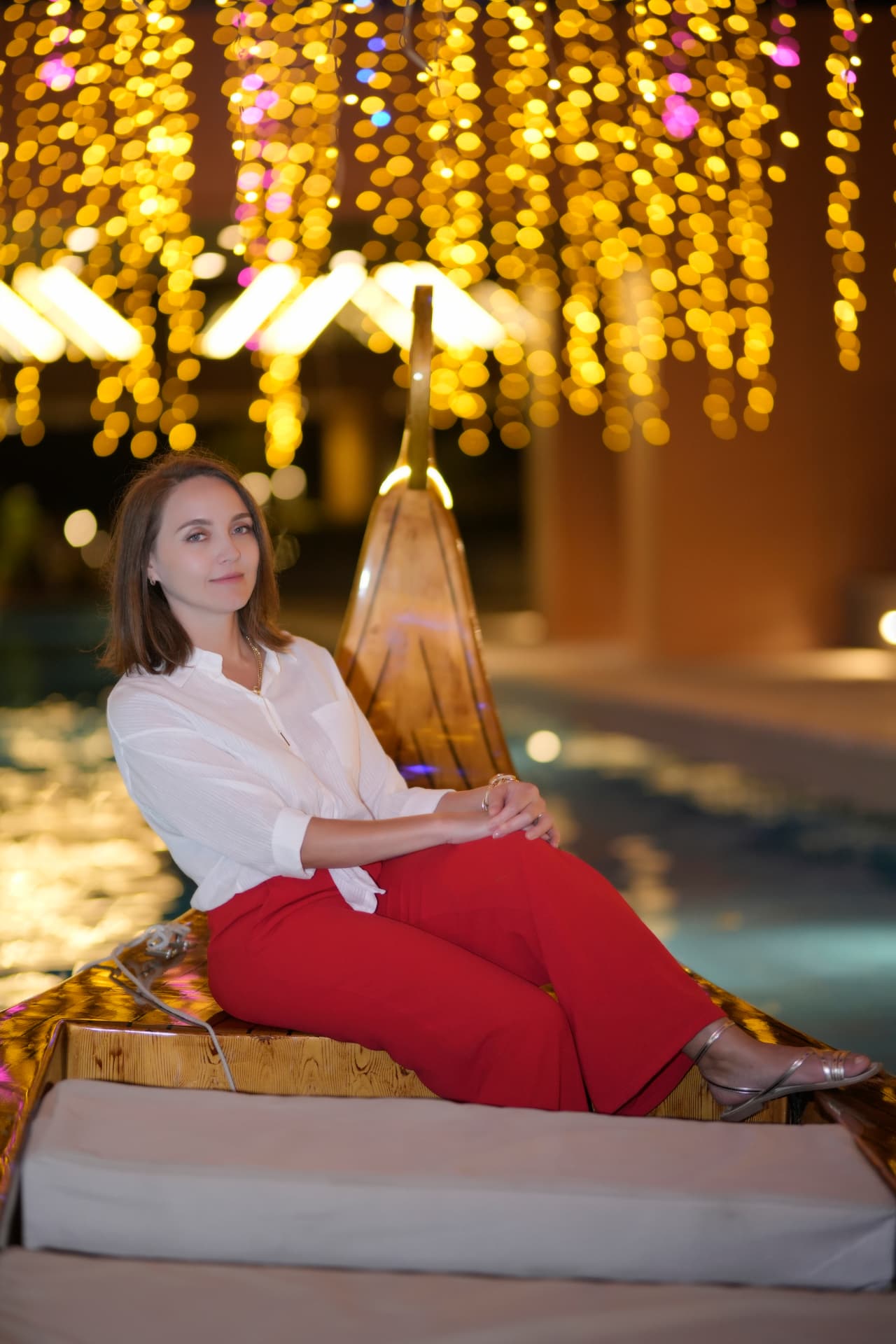 Woman in red trousers seated on a lit gondola at night