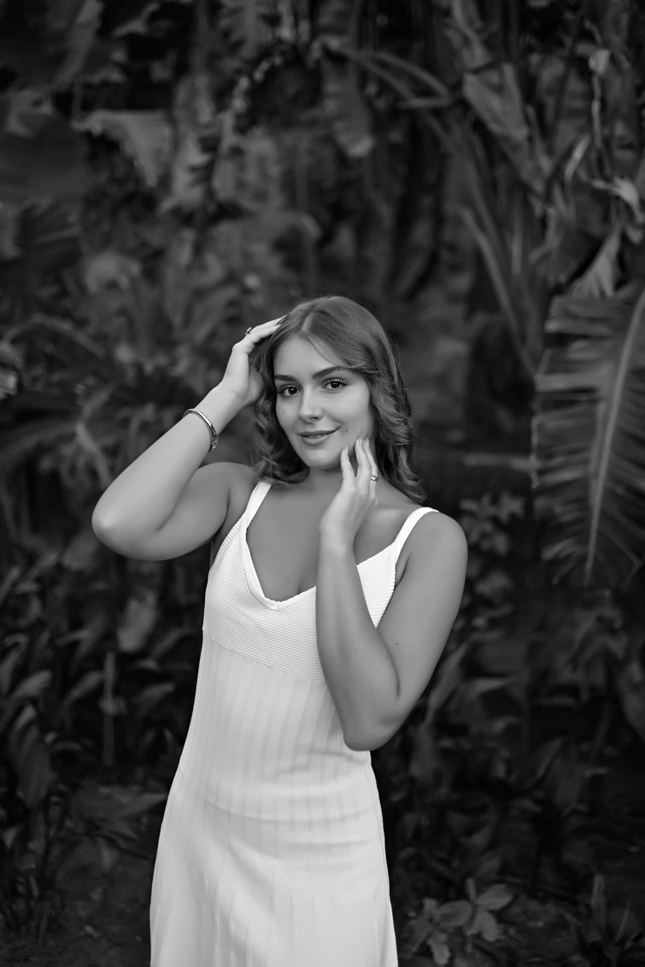Black and white portrait of a woman in a white dress among tropical foliage