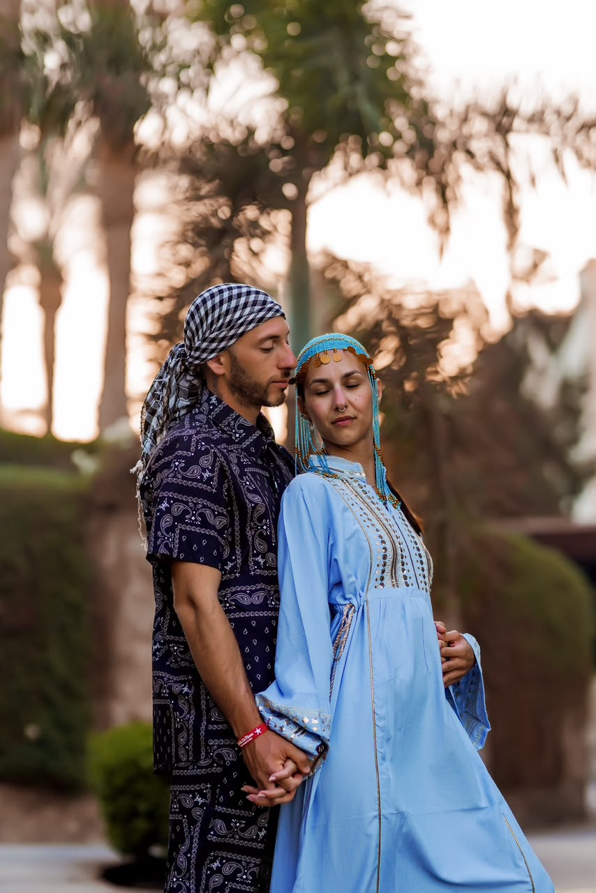 Couple in traditional dress holding hands among palms at sunset