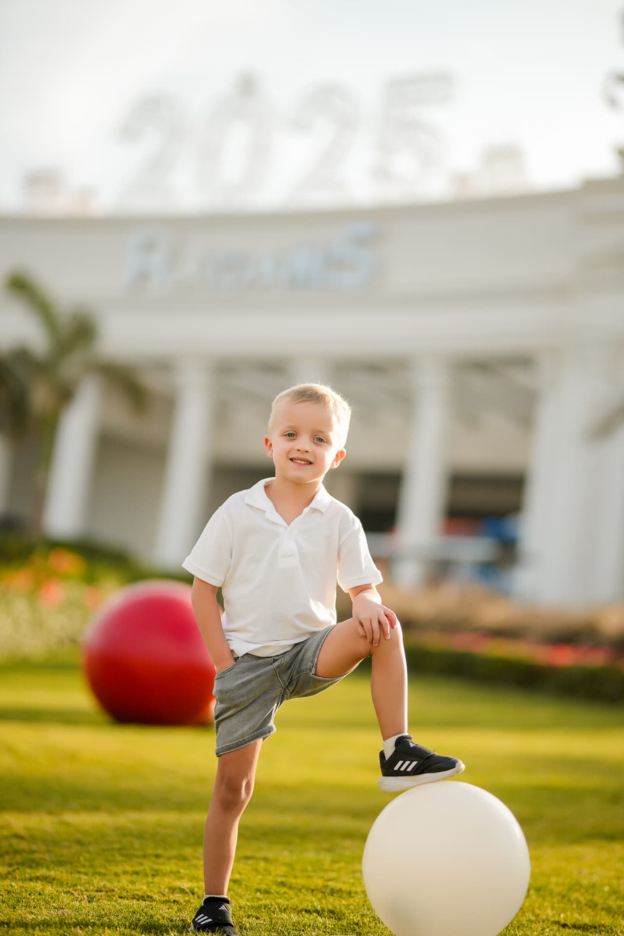 Boy in a white polo resting his foot on a white garden sphere