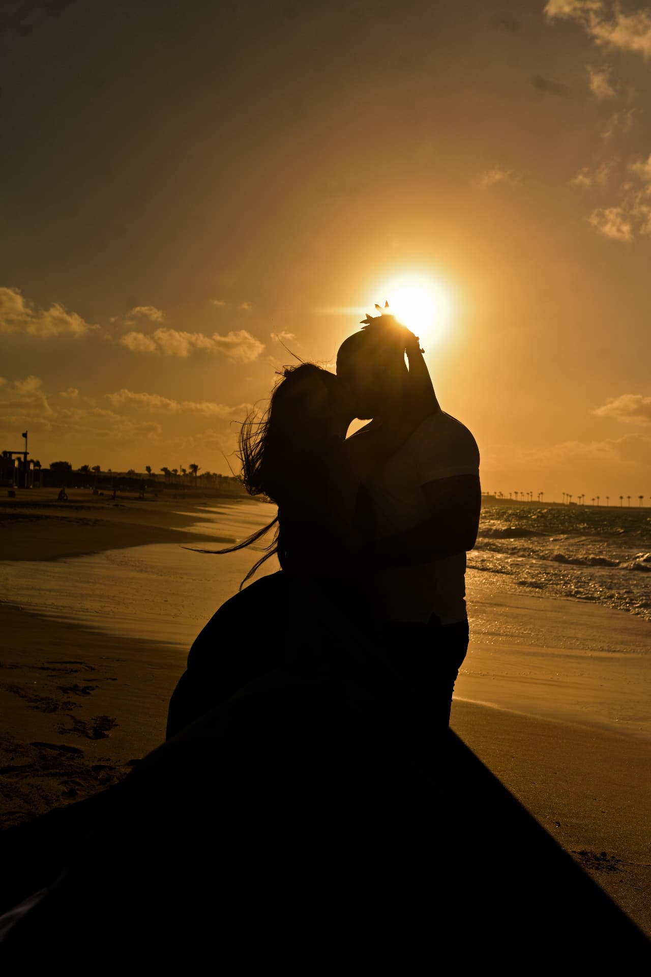 Couple kissing on the beach backlit by a low golden sun