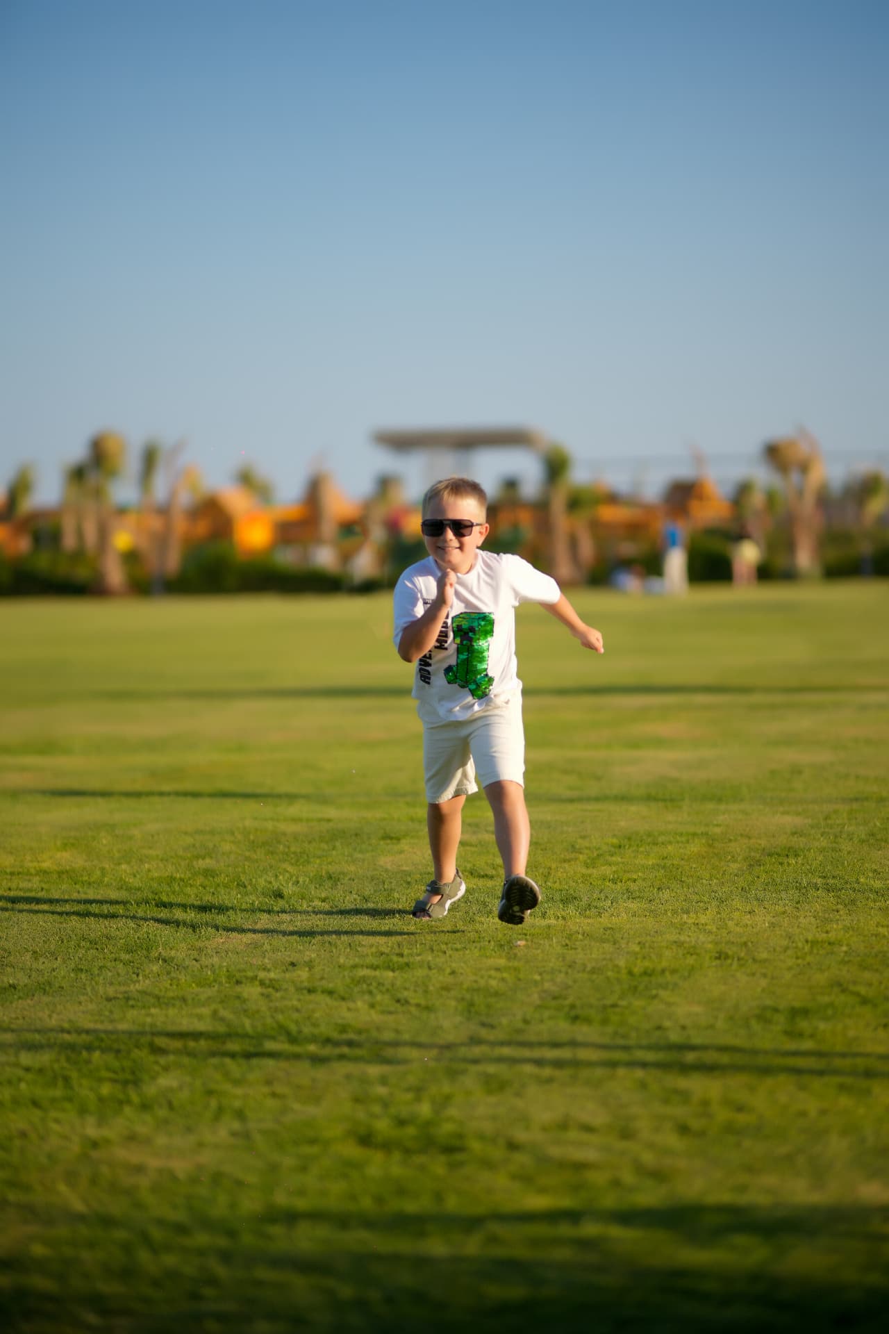 Boy in sunglasses running across a wide green lawn