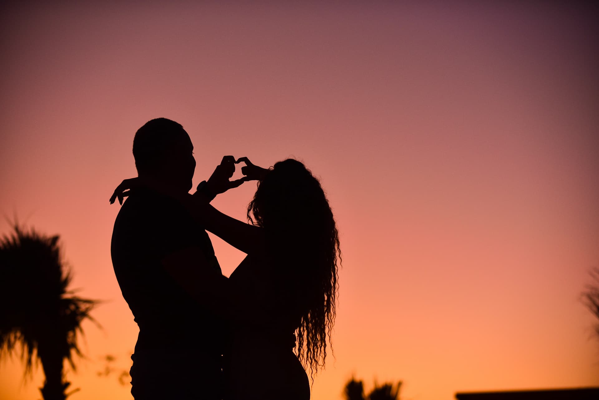Silhouetted couple forming a heart with their hands at twilight