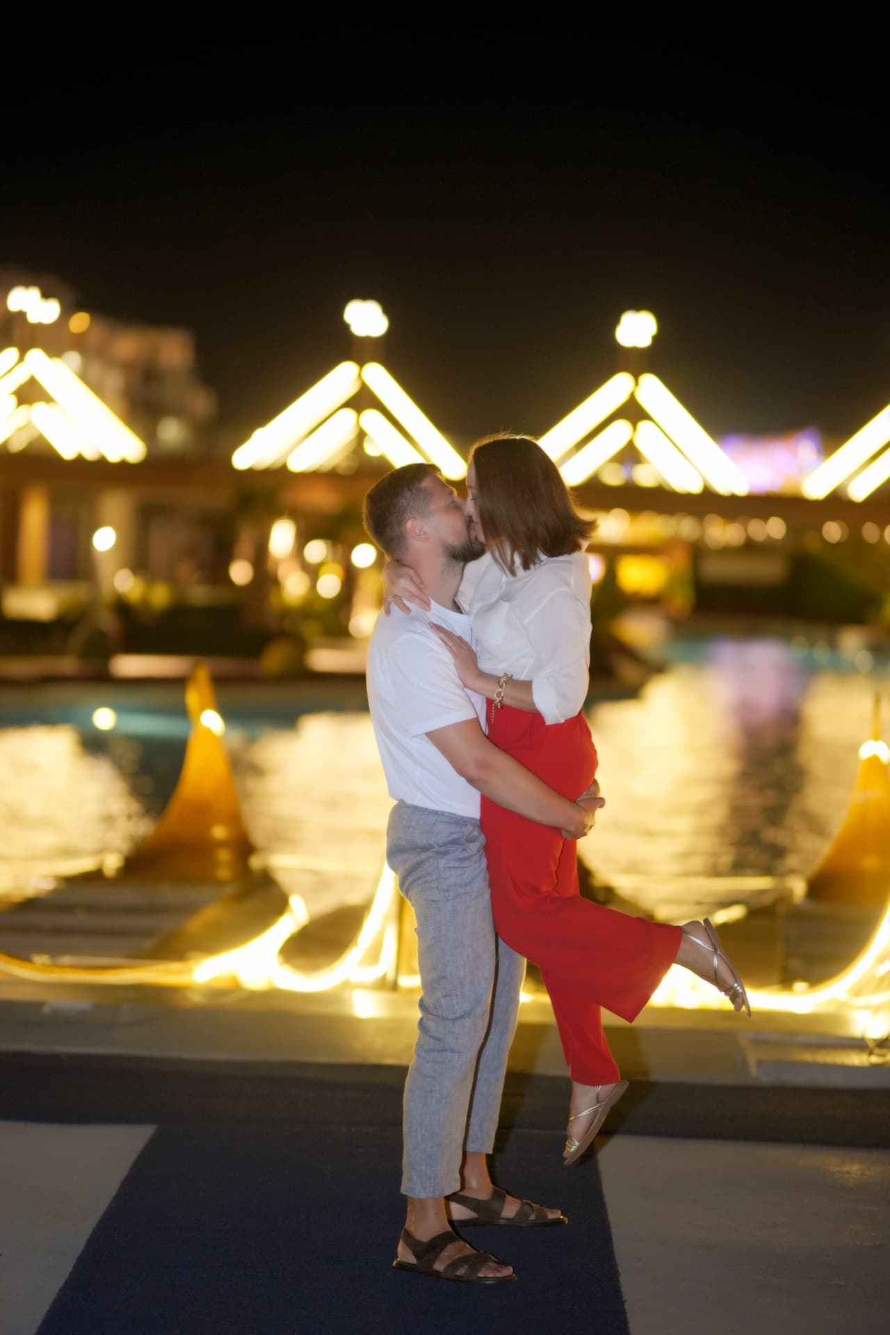Couple kissing in front of glowing night lights by the pool