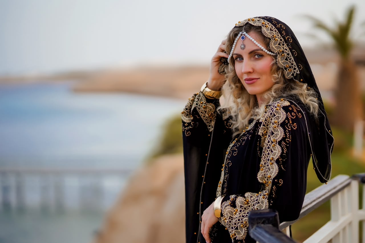 Woman in a black and gold abaya beside a railing overlooking the sea