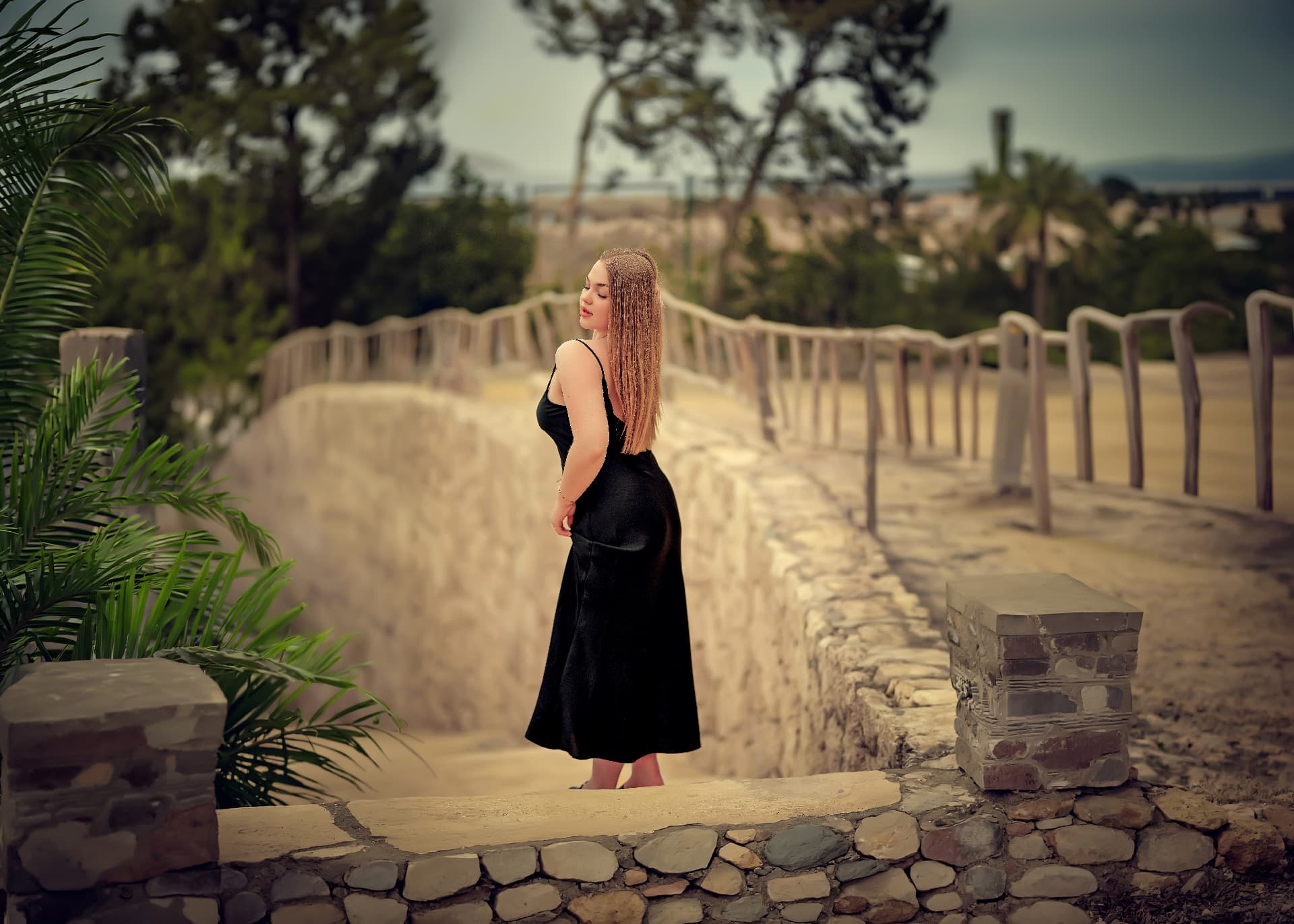 Woman in a black dress on a stone walkway lined with palms