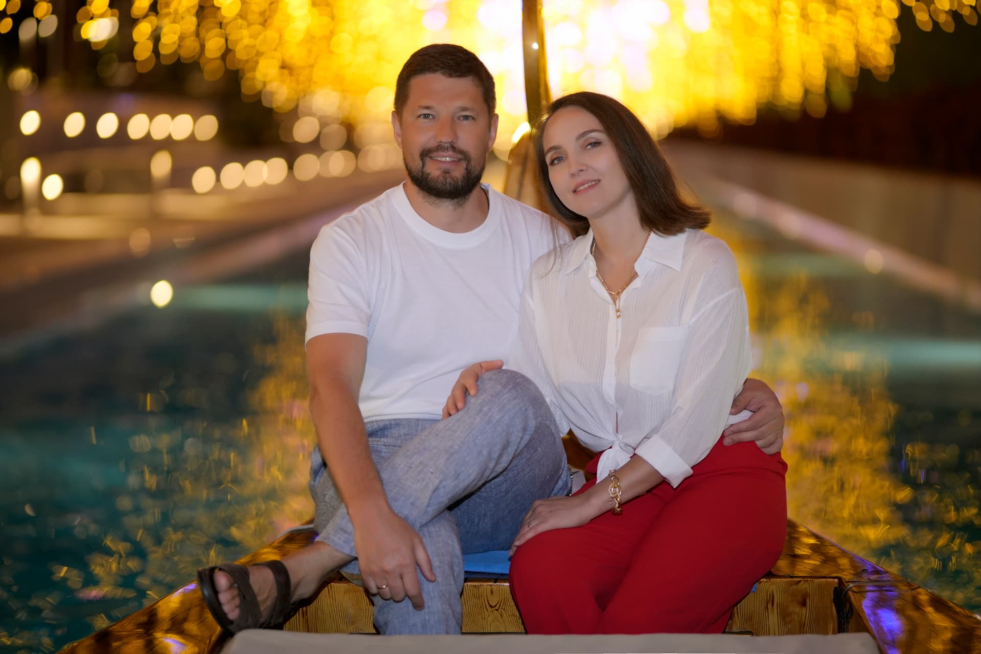 Couple seated together on a wooden boat under warm bokeh lights