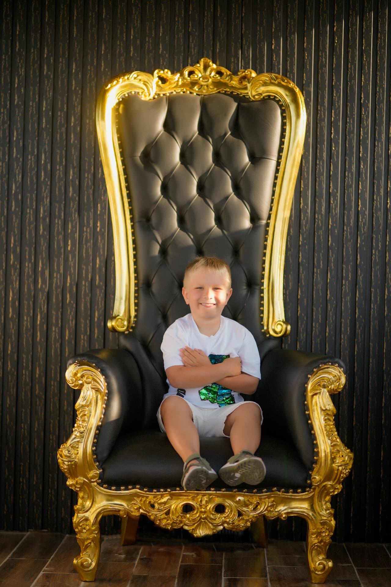 Boy sitting with folded arms on a gold ornate armchair