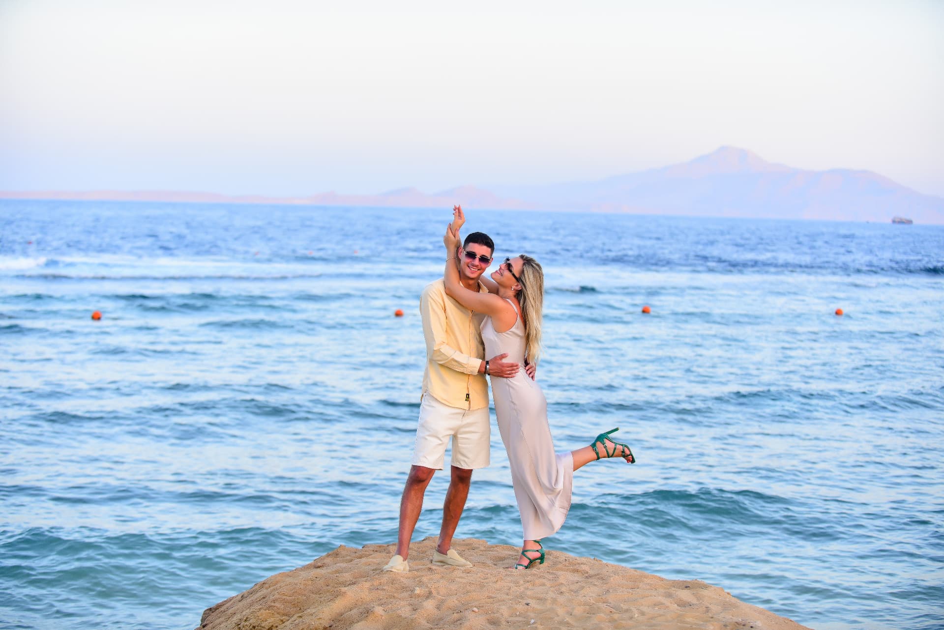 Couple dancing on a rock above the sea with mountains behind
