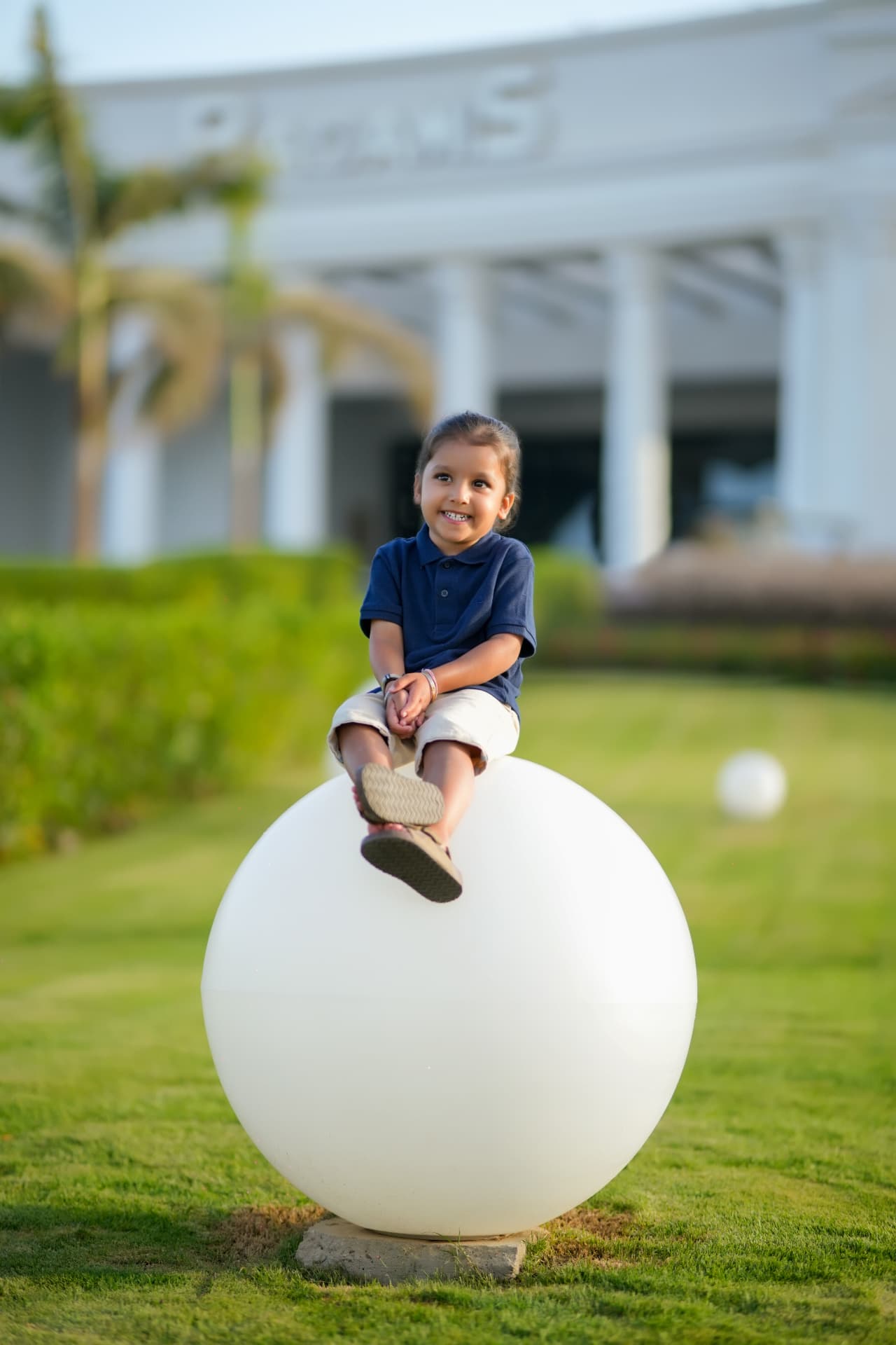 Toddler in a navy polo sitting on a large white garden sphere