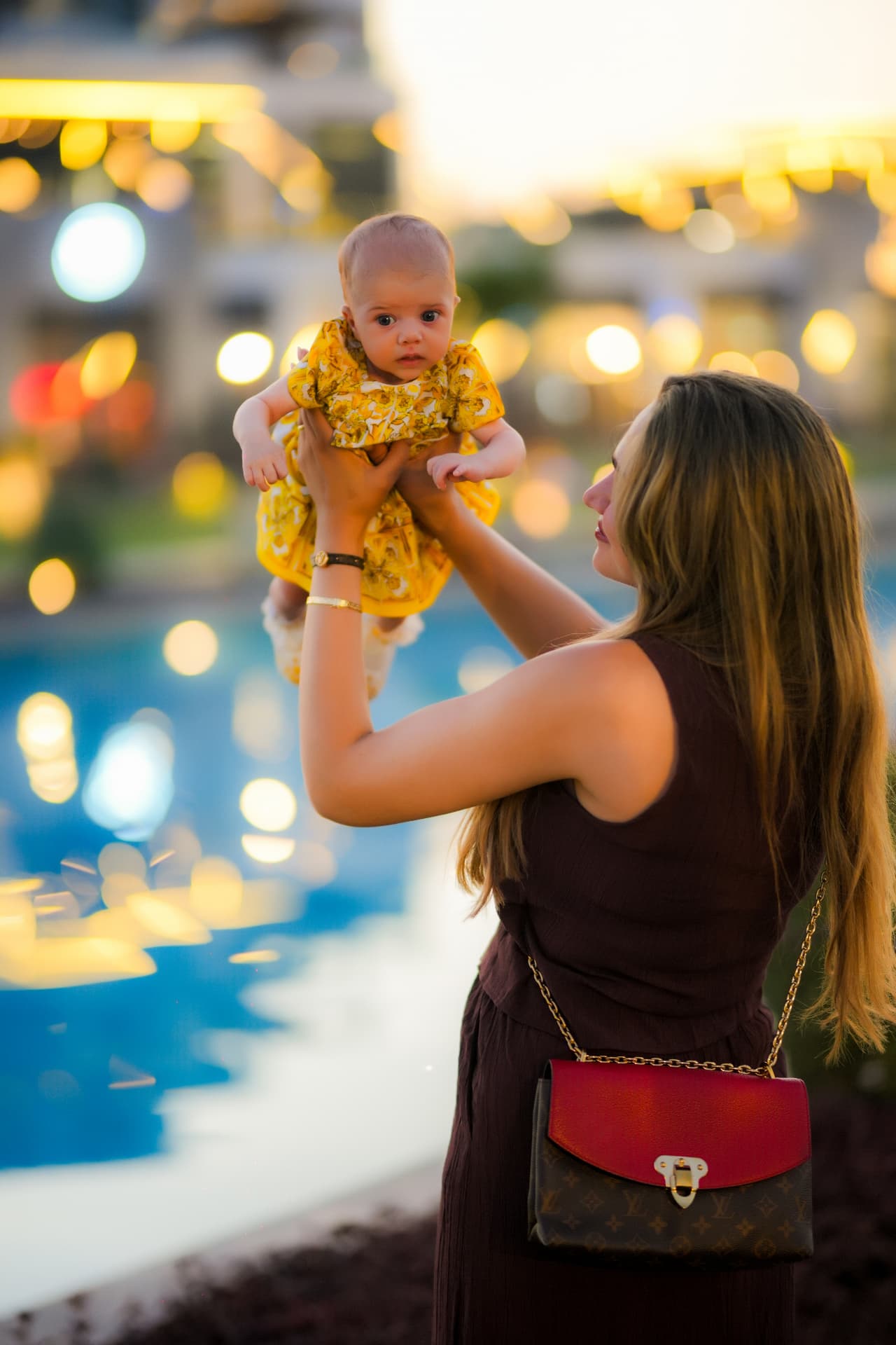 Mother lifting her baby in the air by the pool at golden hour