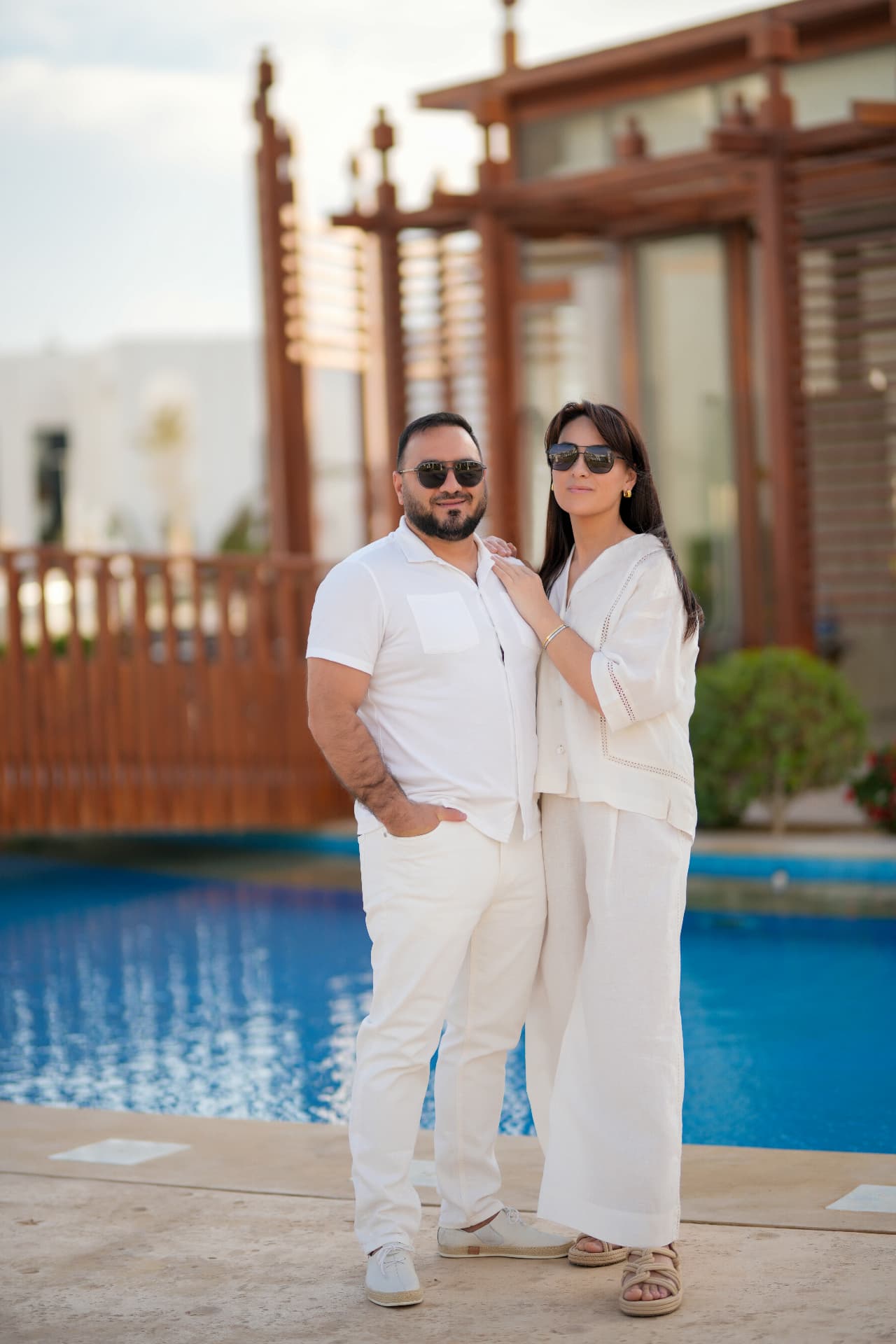 Couple in white linen standing beside a pool at golden hour