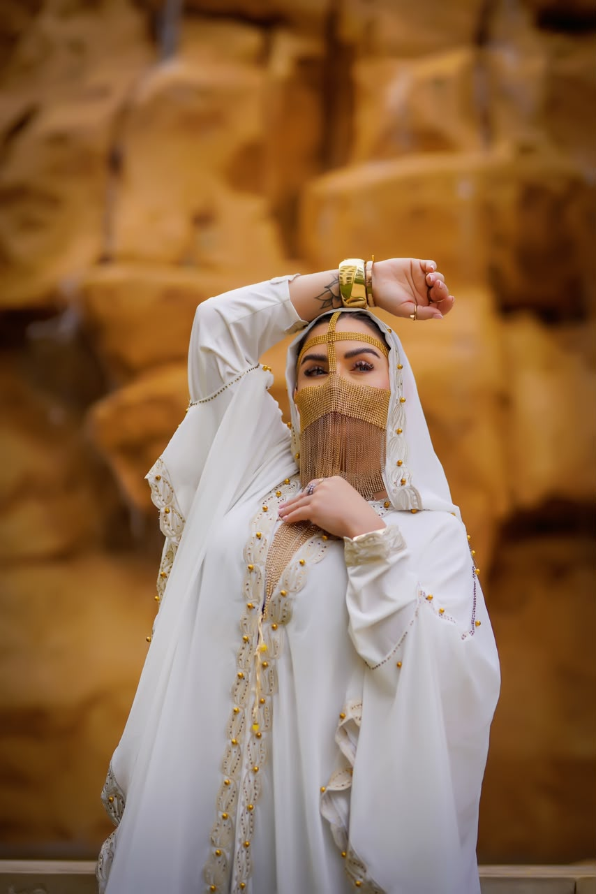 Woman in a white embellished abaya and gold chain veil against desert rock
