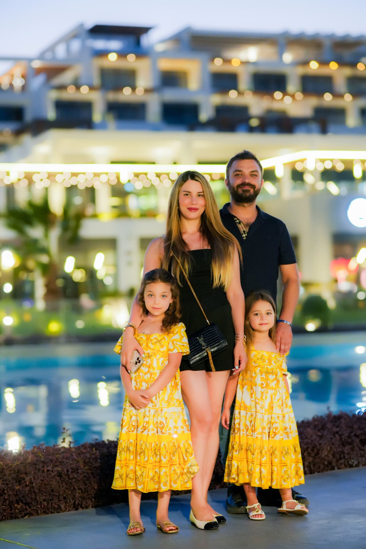 Parents with two daughters in matching yellow dresses at a resort at dusk