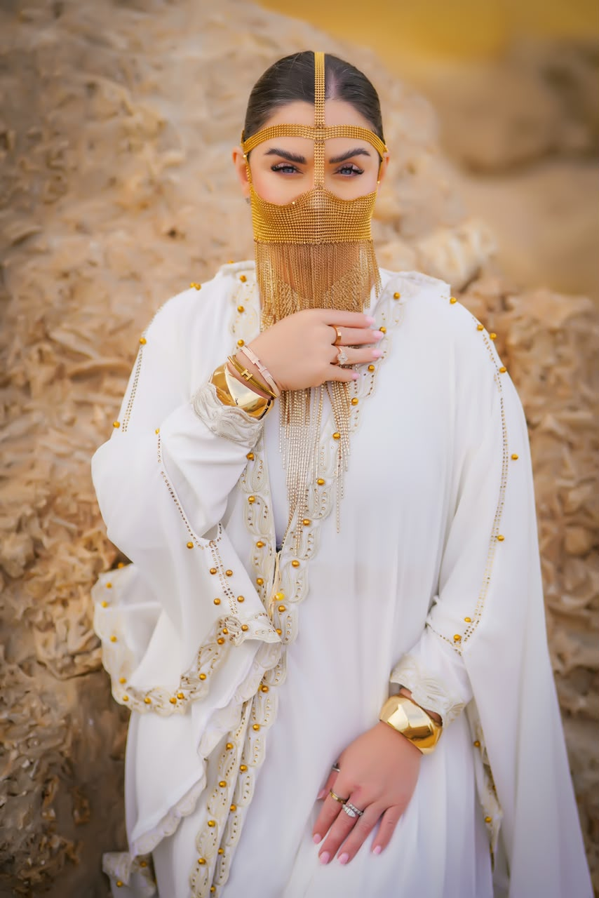 Woman in a white abaya with a gold chain face veil and cuff bracelets