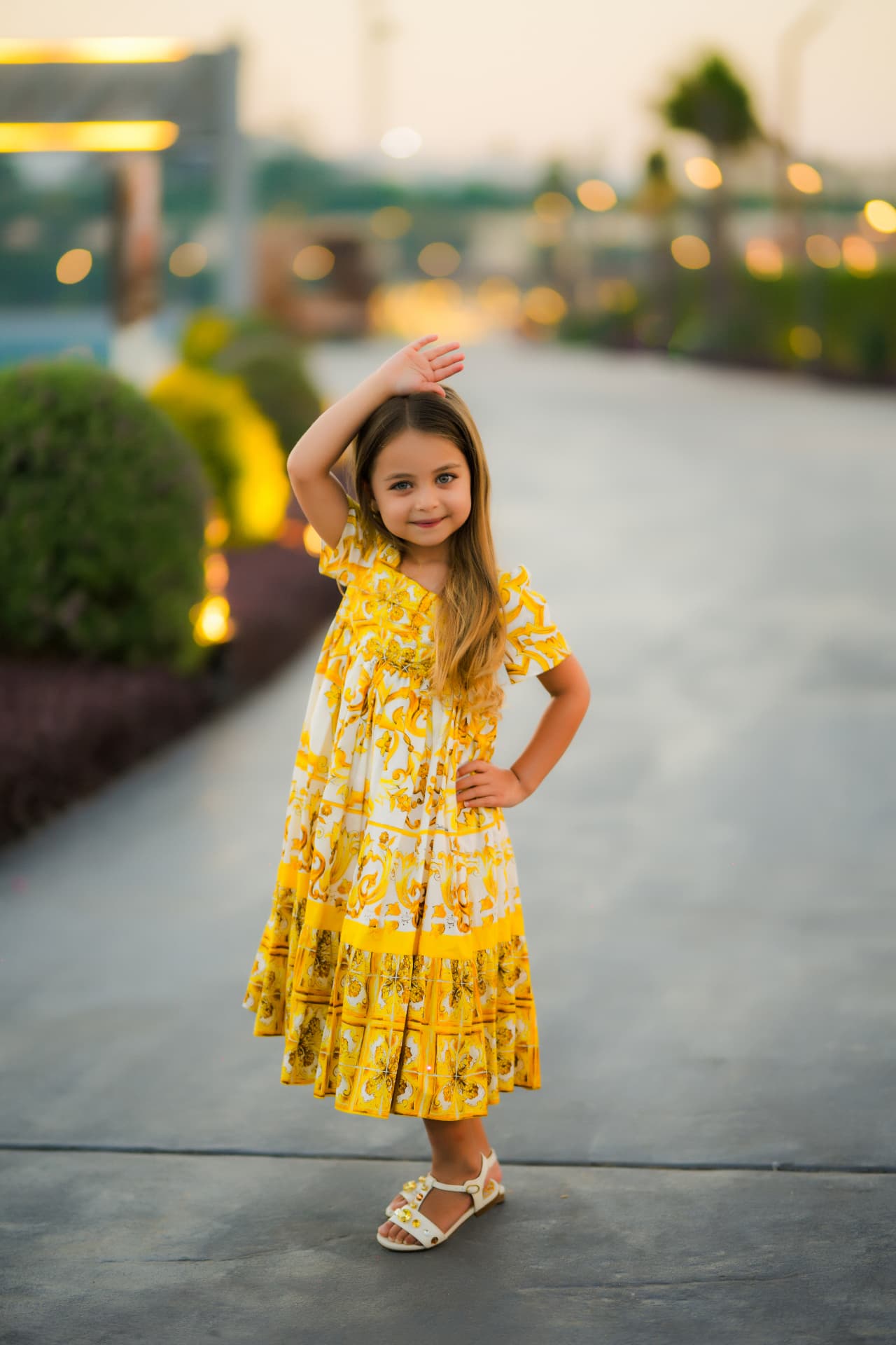 Girl in a yellow print dress posing with warm bokeh lights behind her