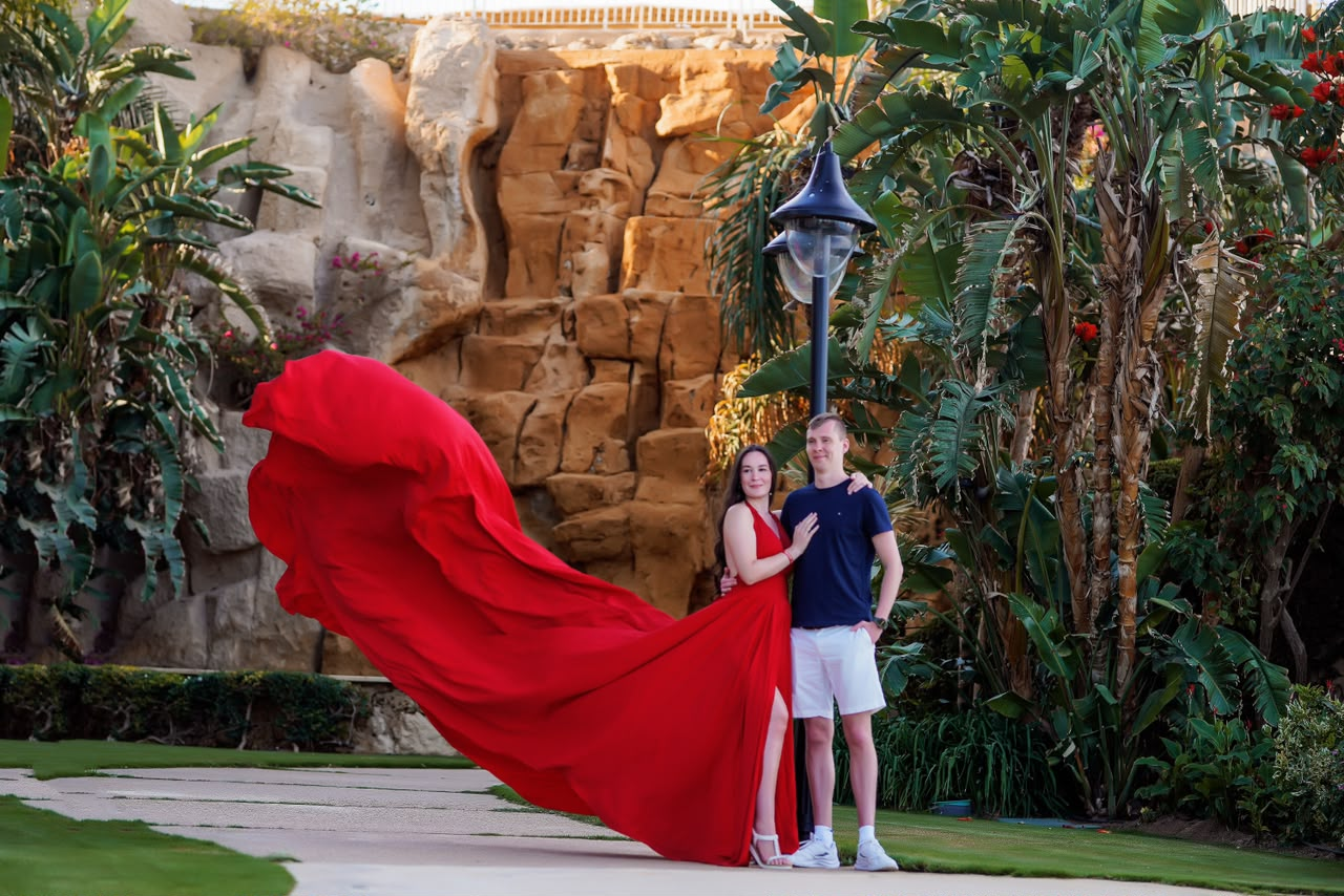 Couple beside a garden lamp, the woman's red gown flowing in the wind
