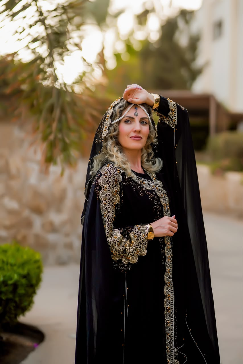 Woman in a black and gold embroidered abaya with a pearl headpiece at sunset