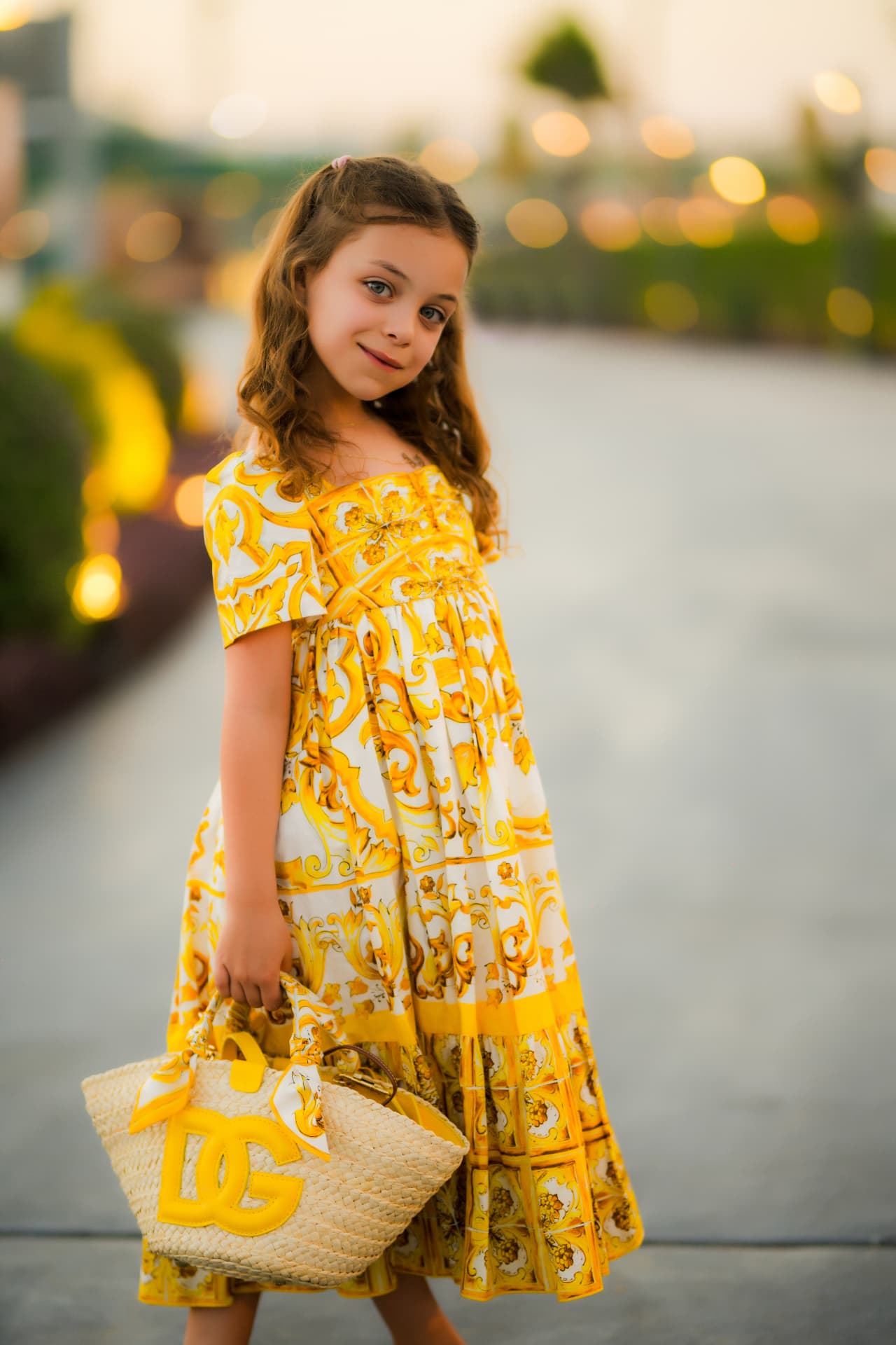 Girl in a yellow print dress holding a woven basket bag at sunset