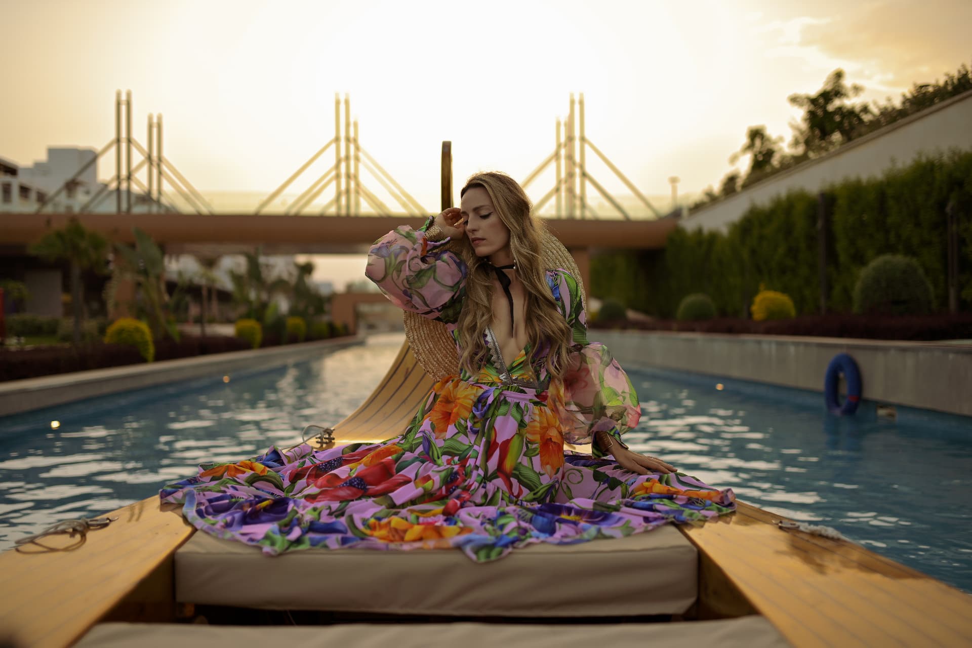 Woman in a floral gown seated on a wooden boat at sunset