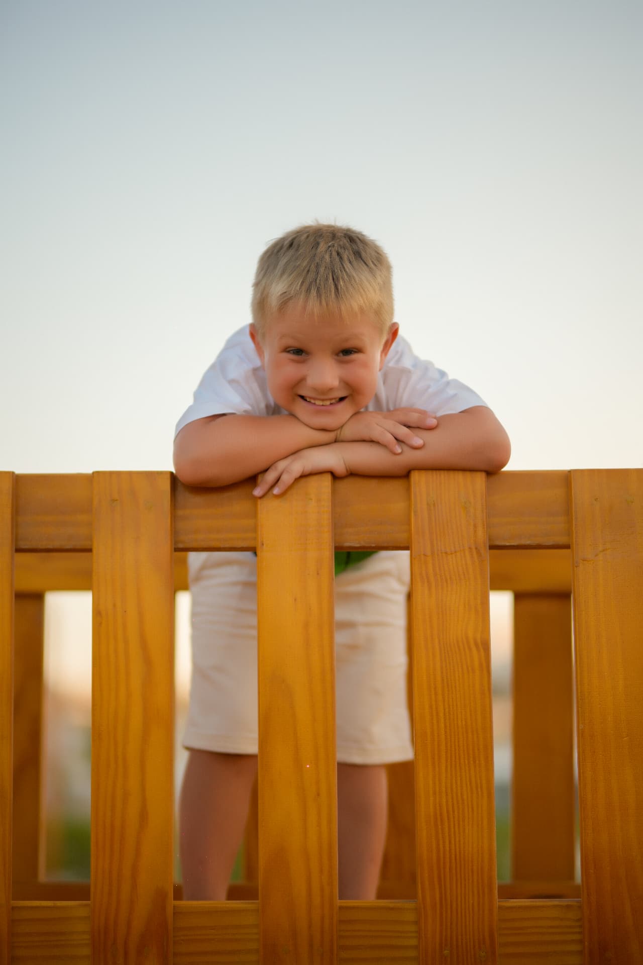 Boy leaning over a wooden fence smiling at the camera