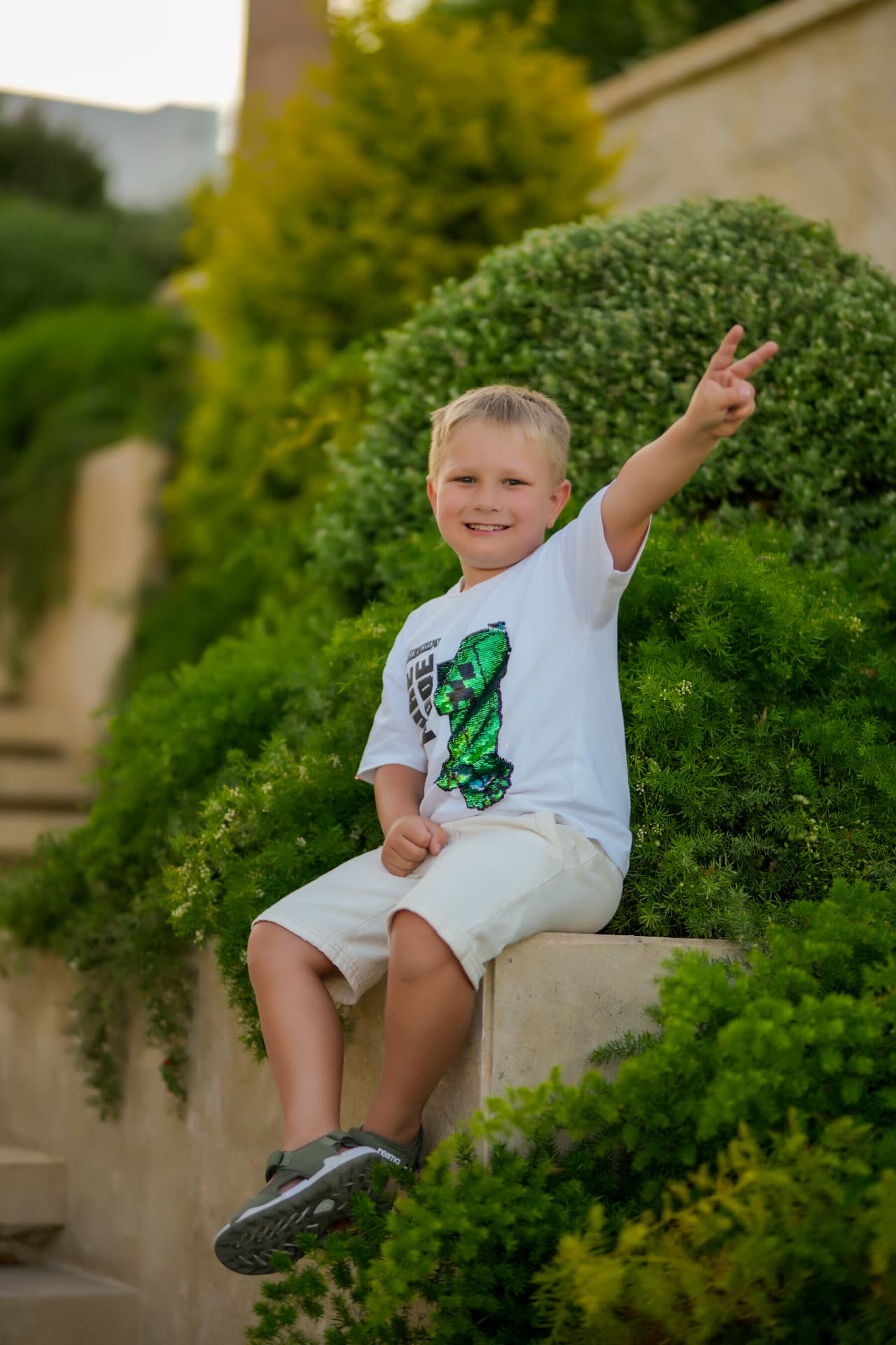 Boy sitting on a garden wall making a peace sign