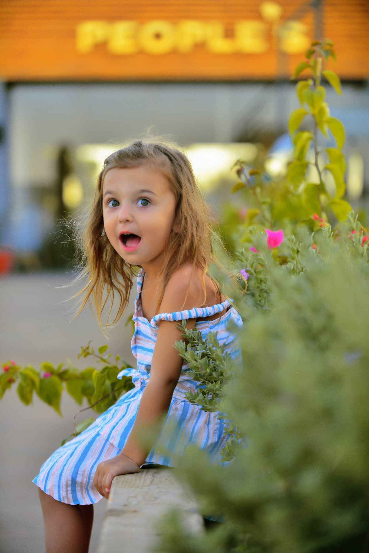 Girl in a striped dress with a surprised expression beside flowers