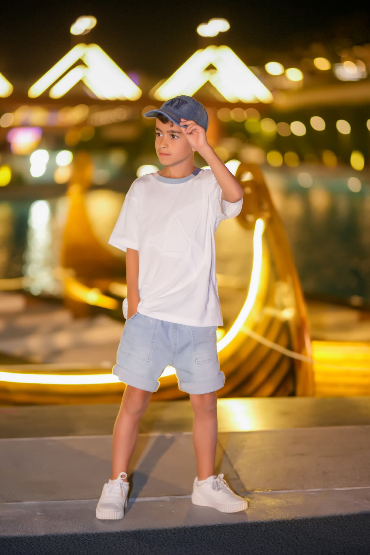 Boy in a denim cap posing by illuminated resort canals at night