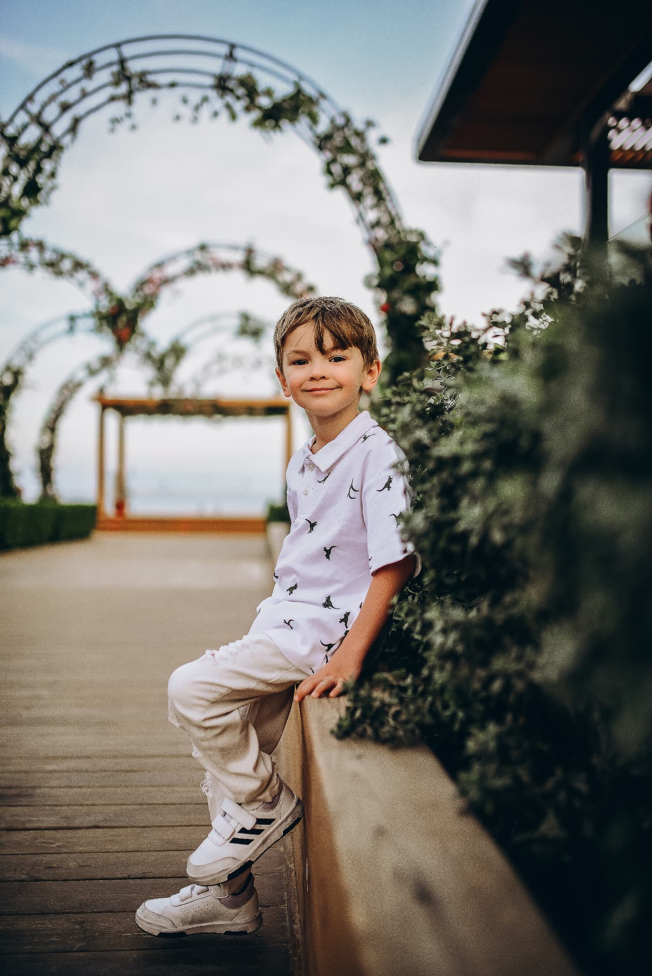 Boy sitting on a low wall in front of floral garden arches