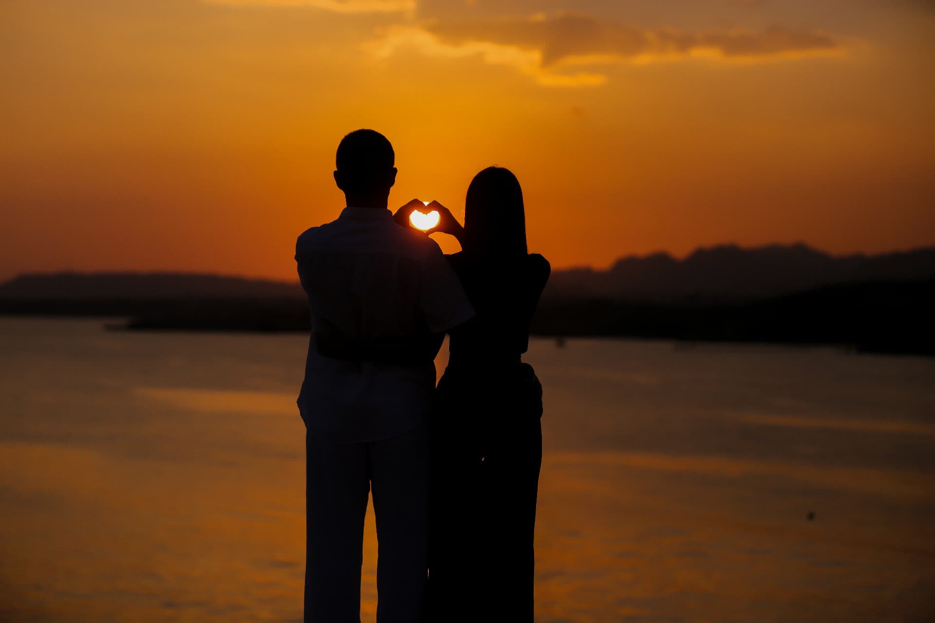 Couple framing the setting sun with their hands in a heart shape