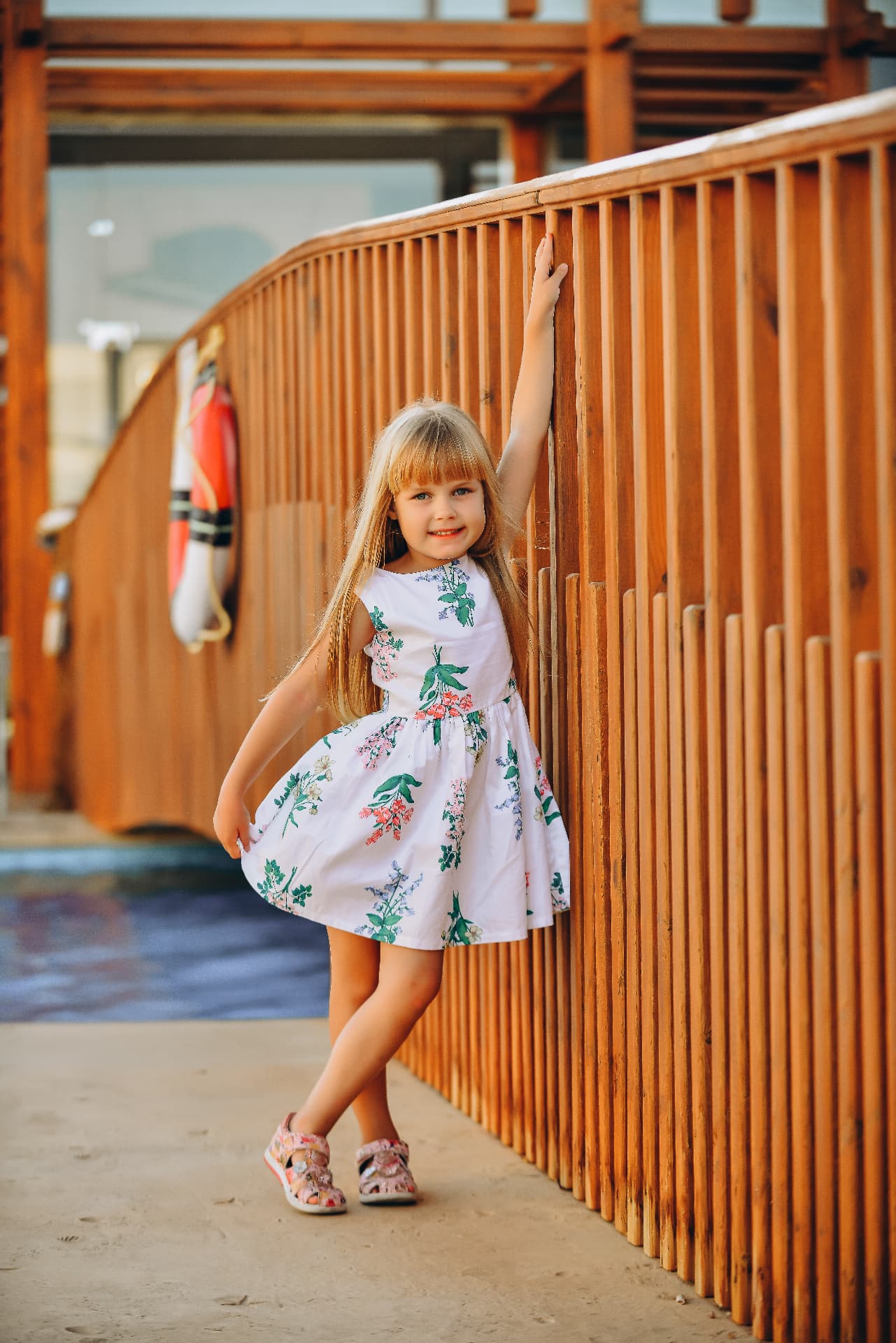 Girl in a floral dress posing against a curved wooden railing