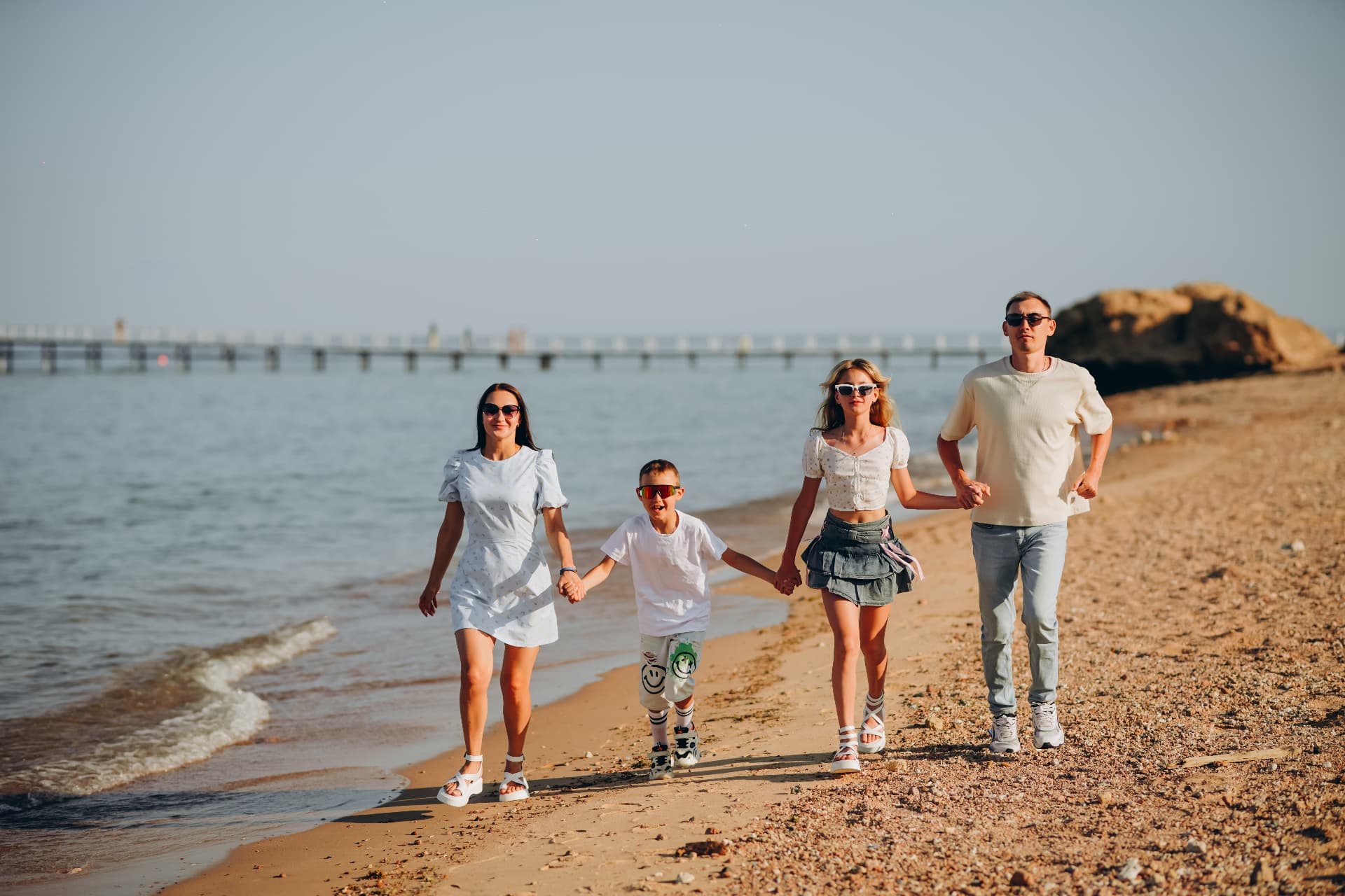 Family of four walking hand in hand along the shoreline at golden hour