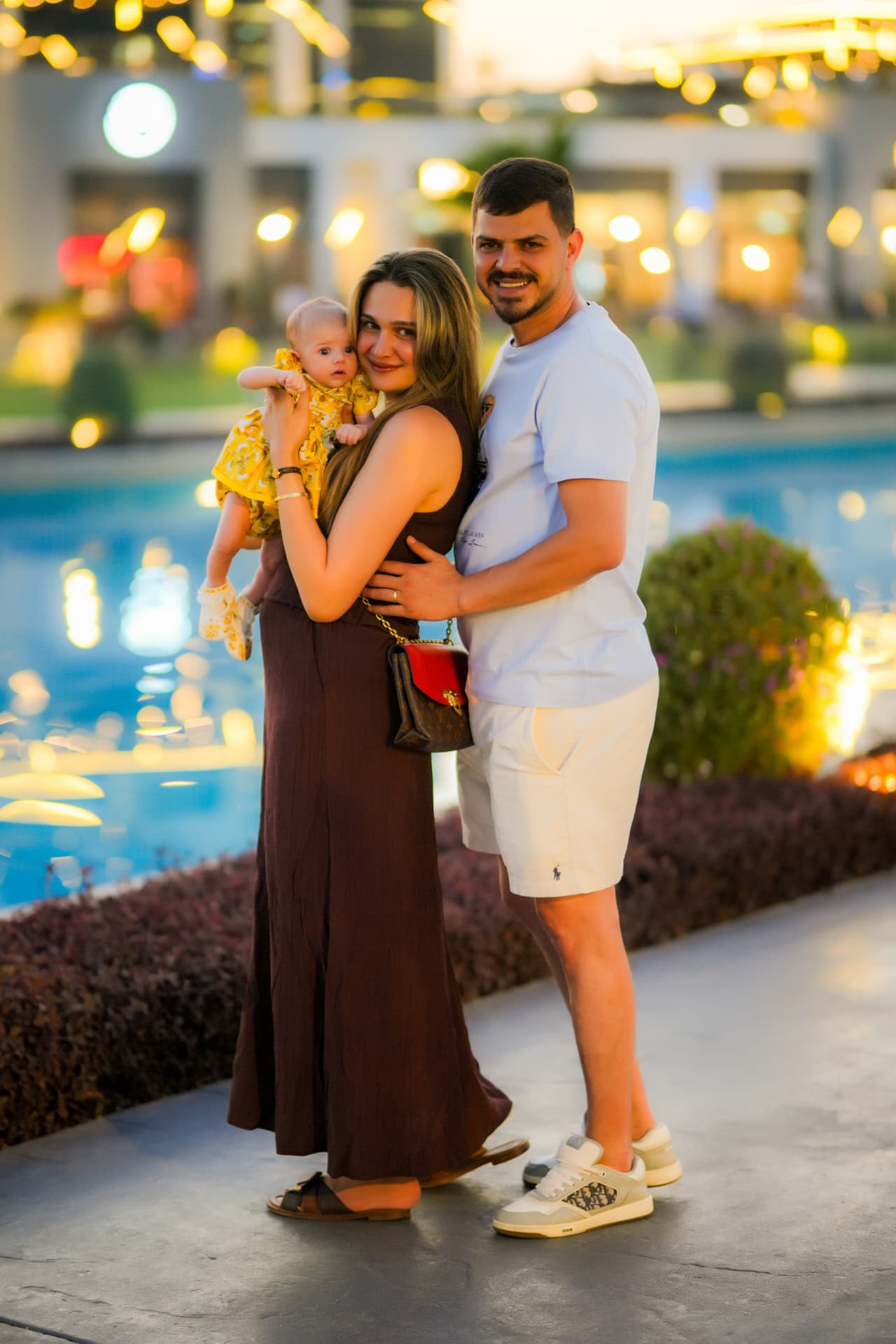 Parents holding their baby together in front of a pool at dusk