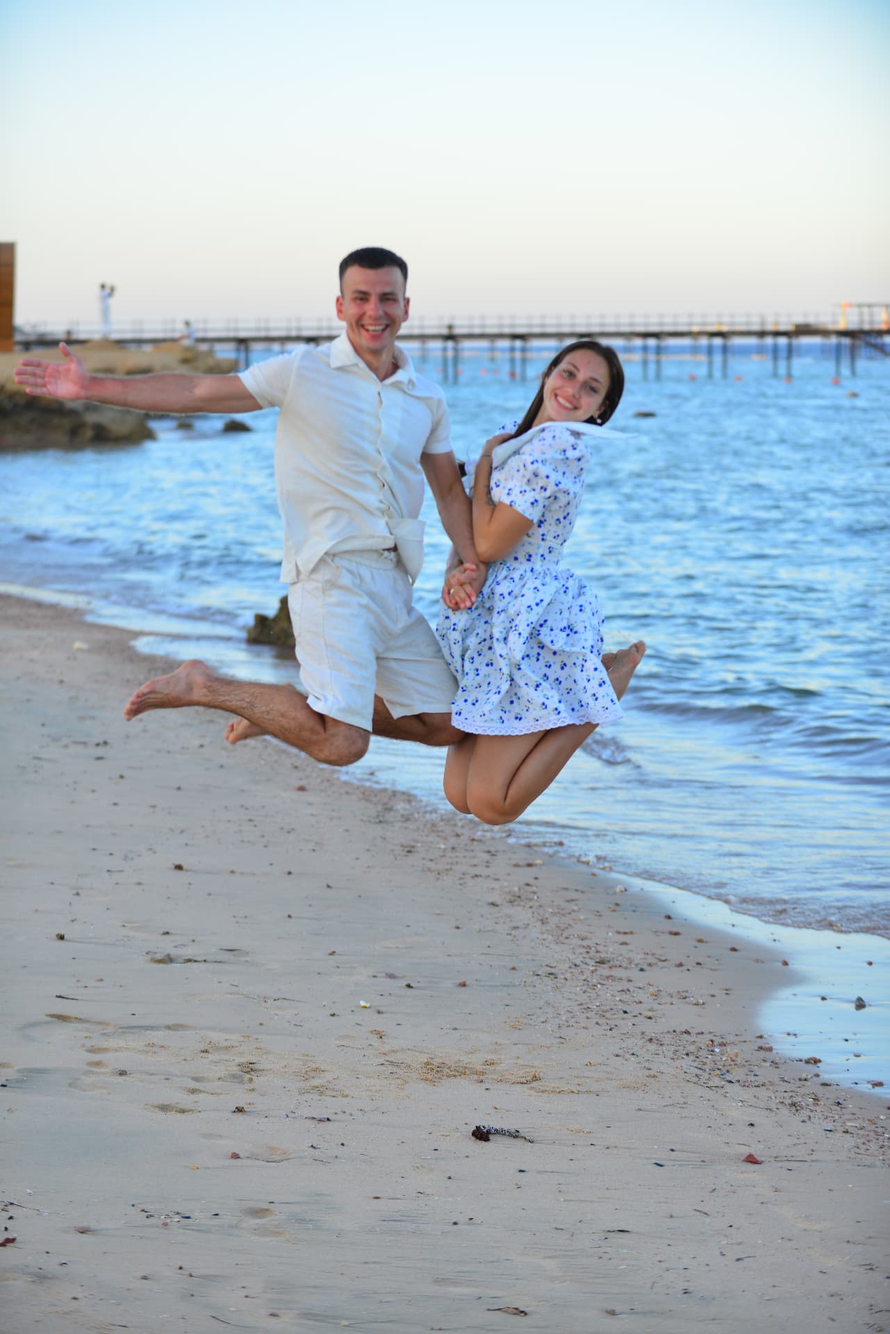 Couple jumping hand in hand on the sand at dusk