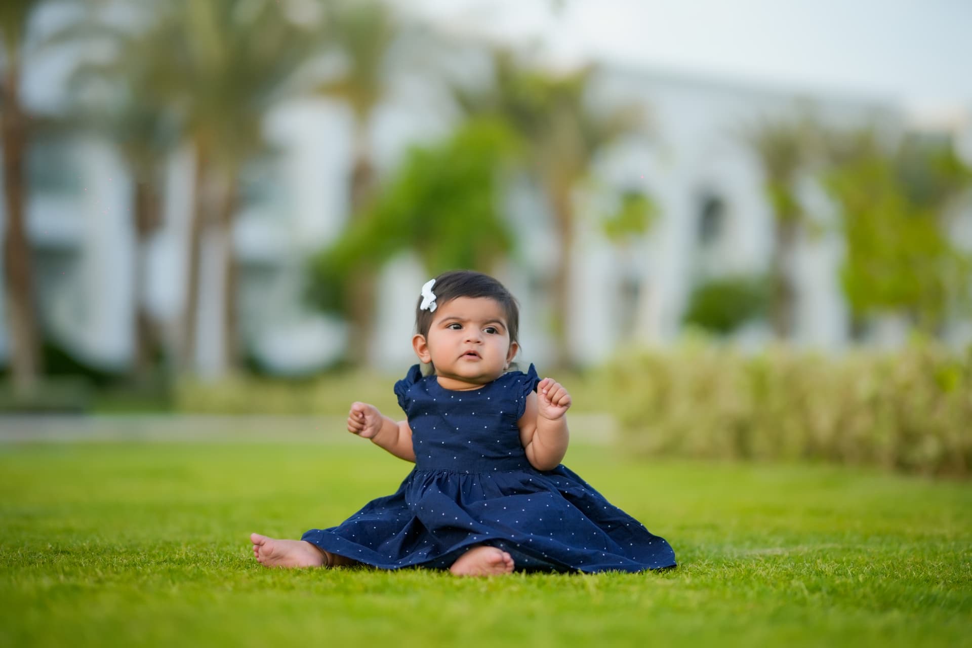 Baby girl in a navy polka dot dress sitting on a green lawn