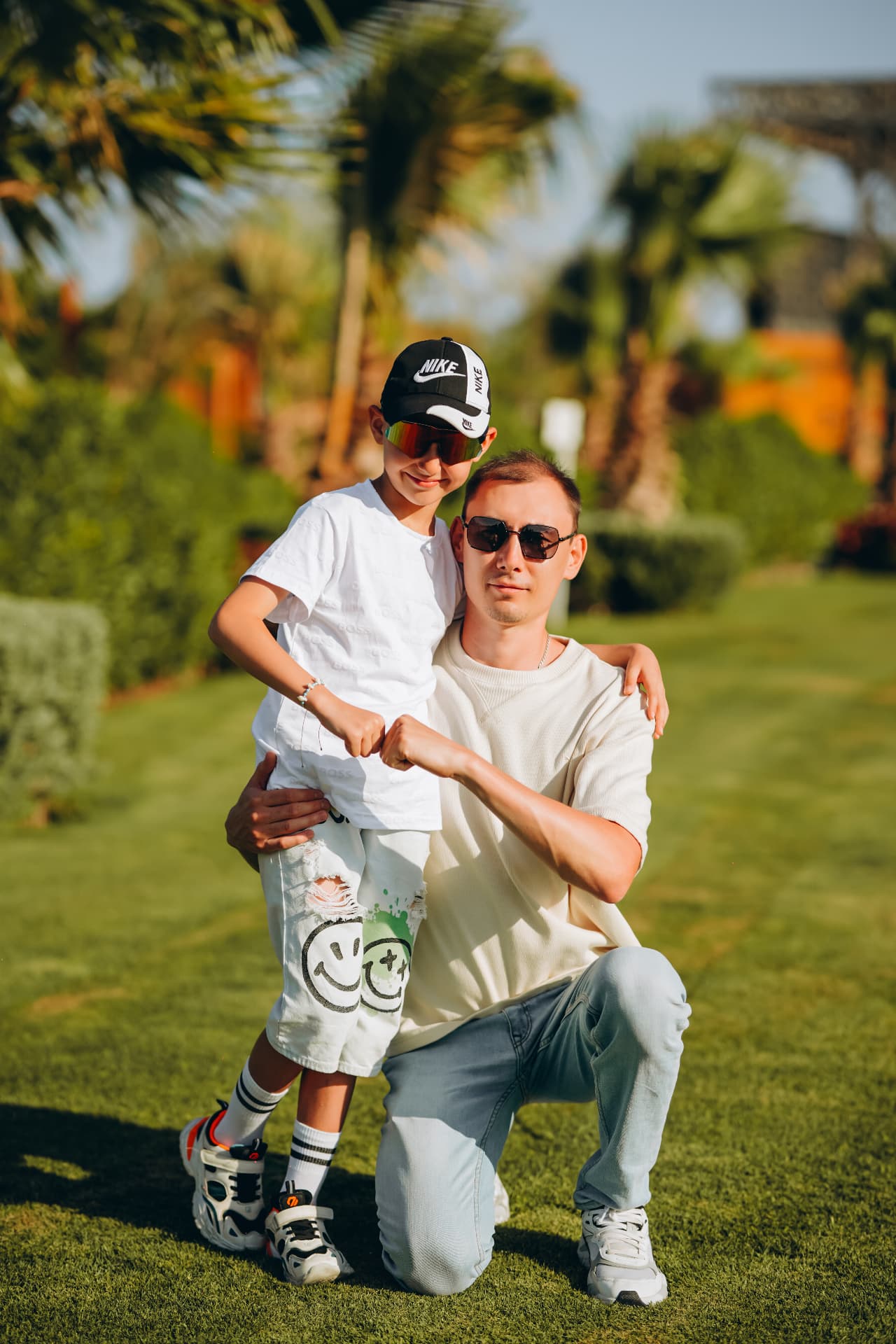 Father kneeling on the grass with his son among palm trees