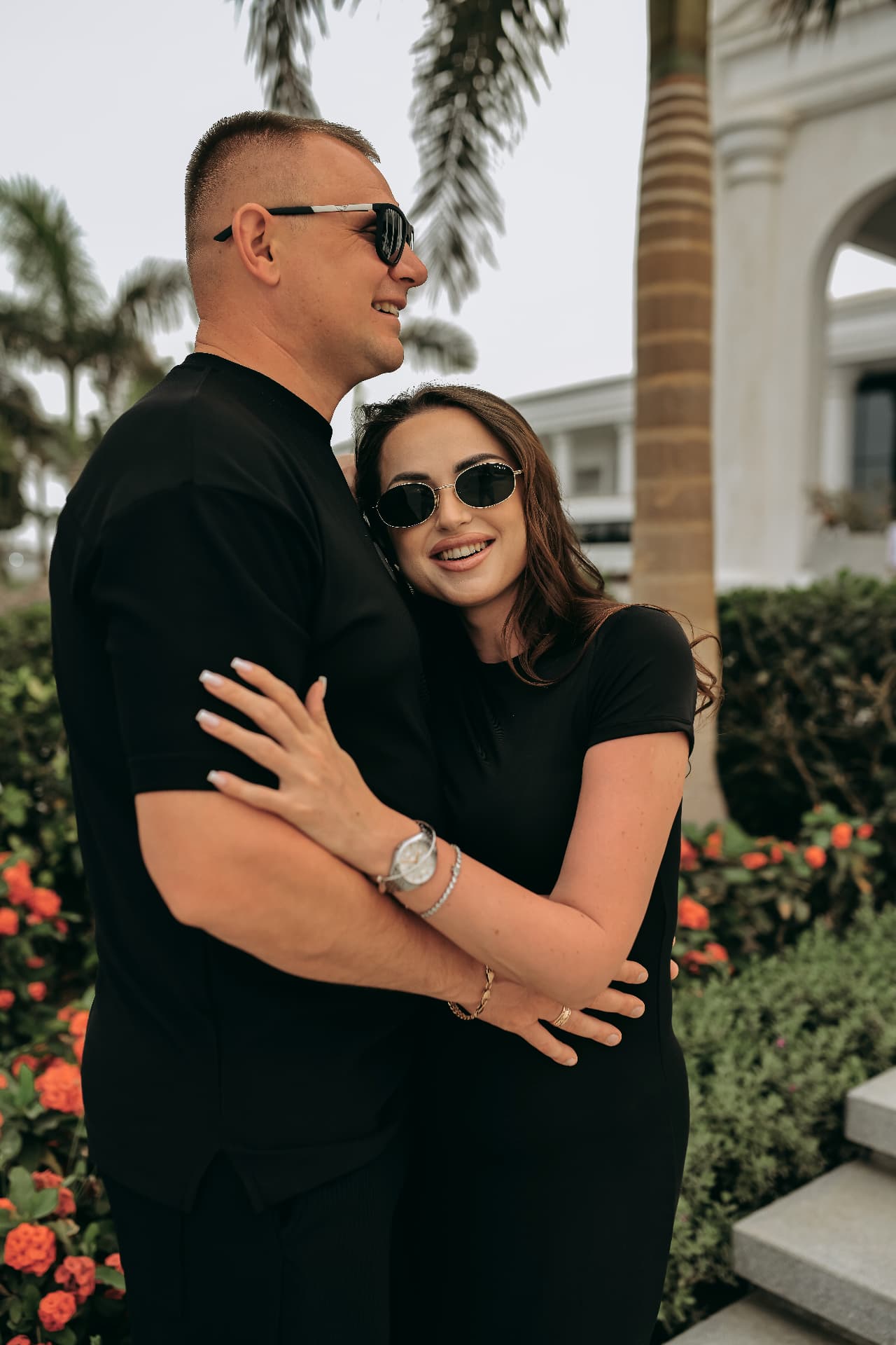 Couple in black embracing and laughing under palm trees