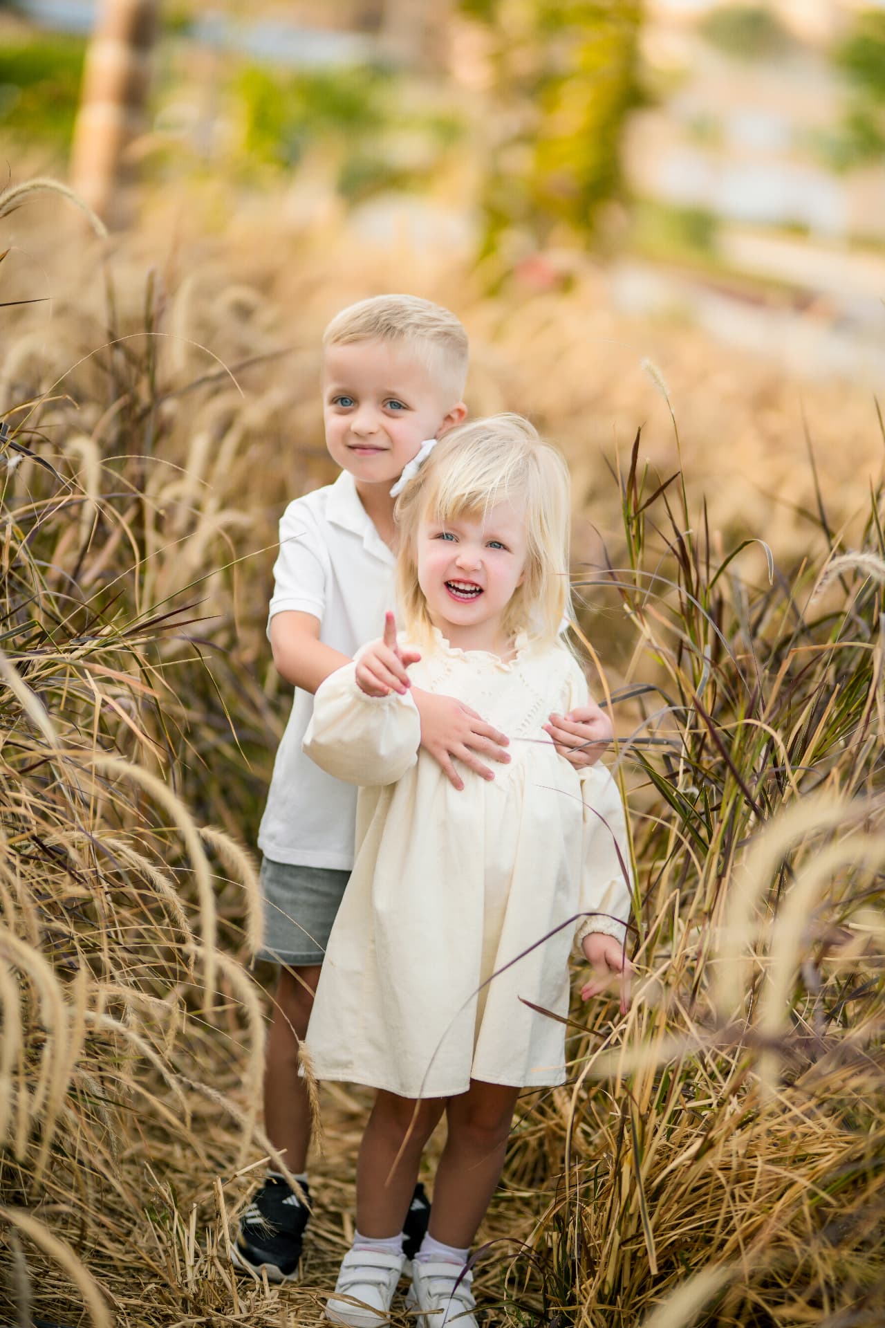 Brother hugging his laughing sister among tall ornamental grasses
