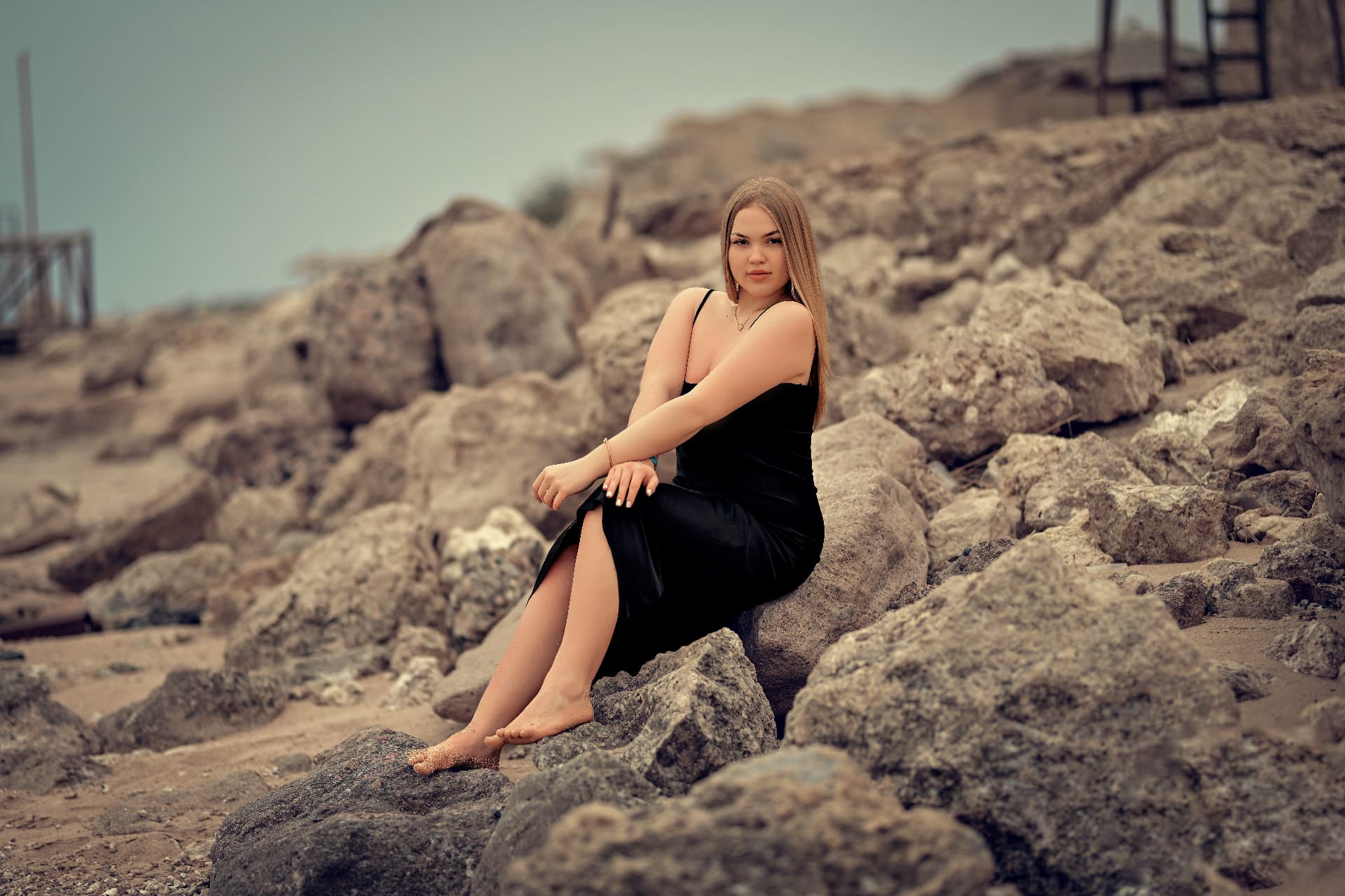 Woman in a black dress seated on coastal rocks
