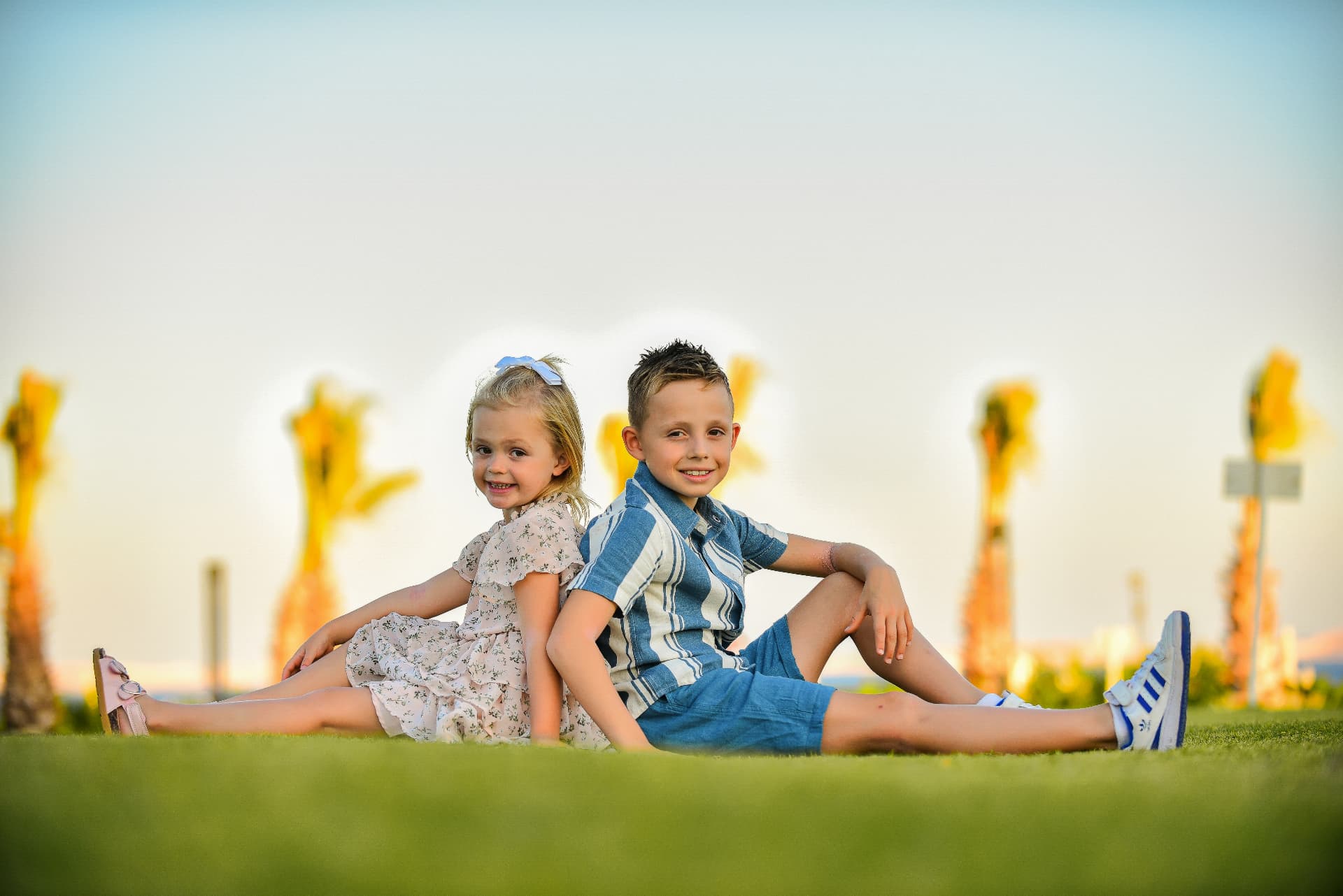 Brother and sister sitting back to back on a lawn at sunset