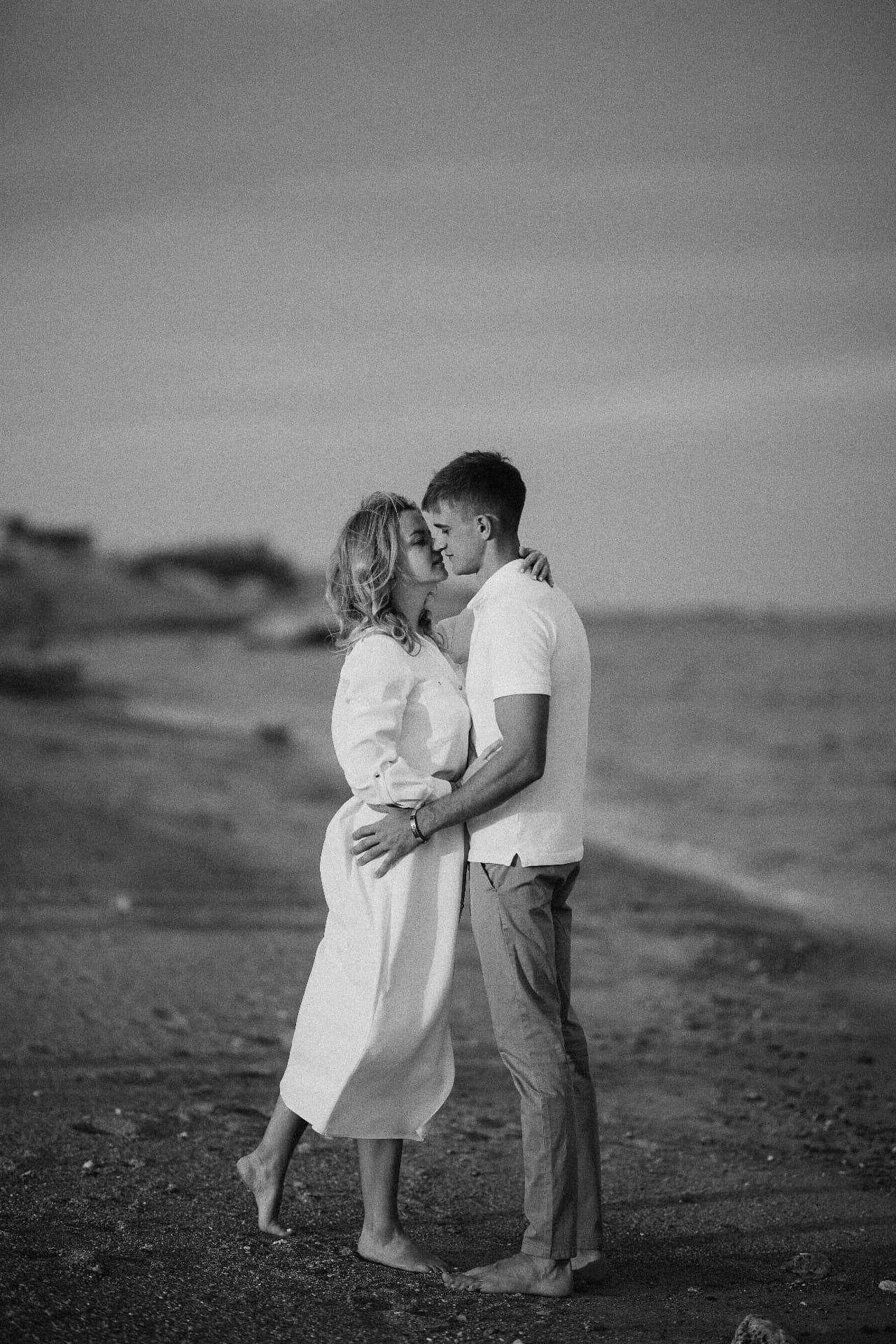 Black and white portrait of a couple embracing on a quiet shoreline