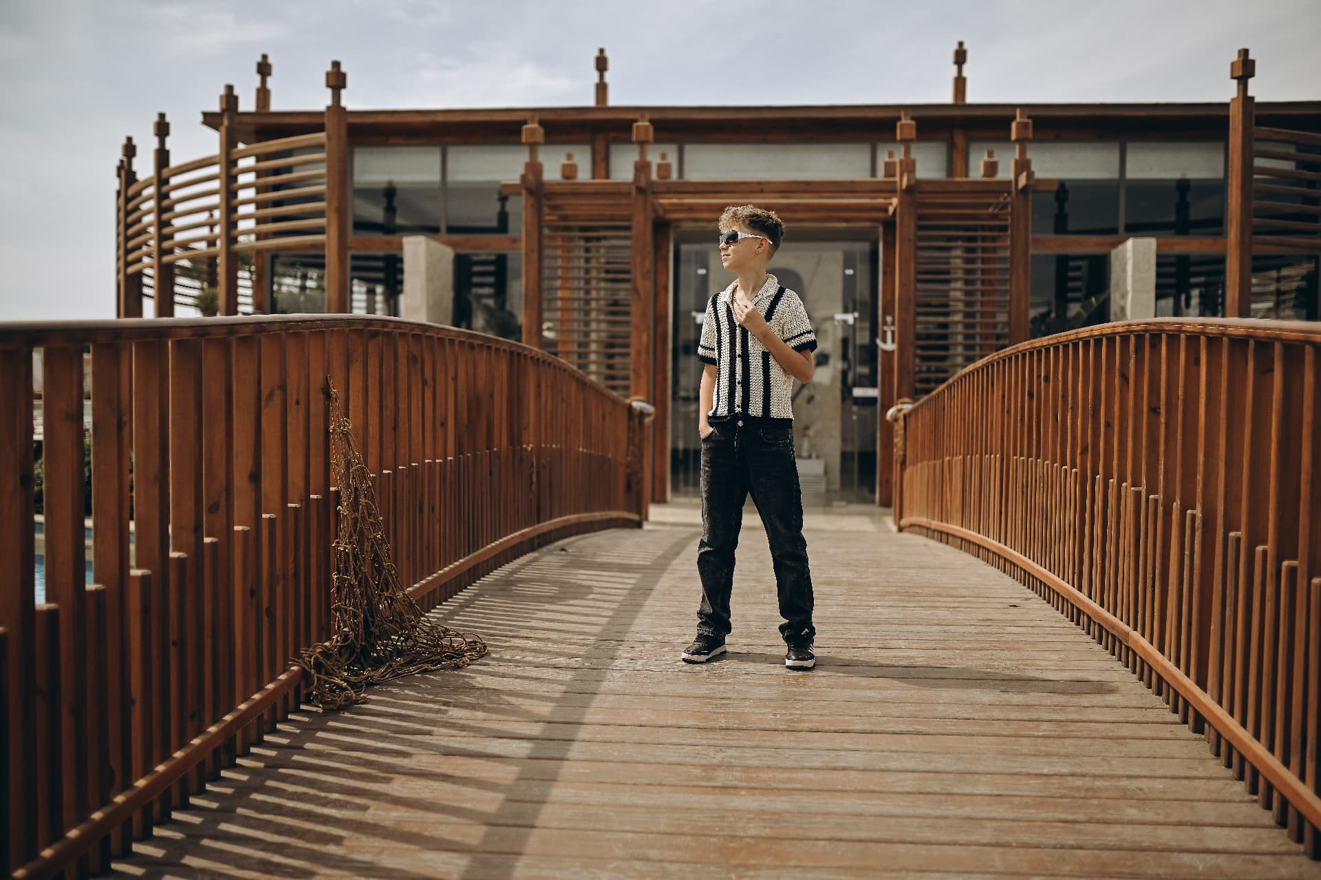 Boy in sunglasses standing on a wooden bridge by the water